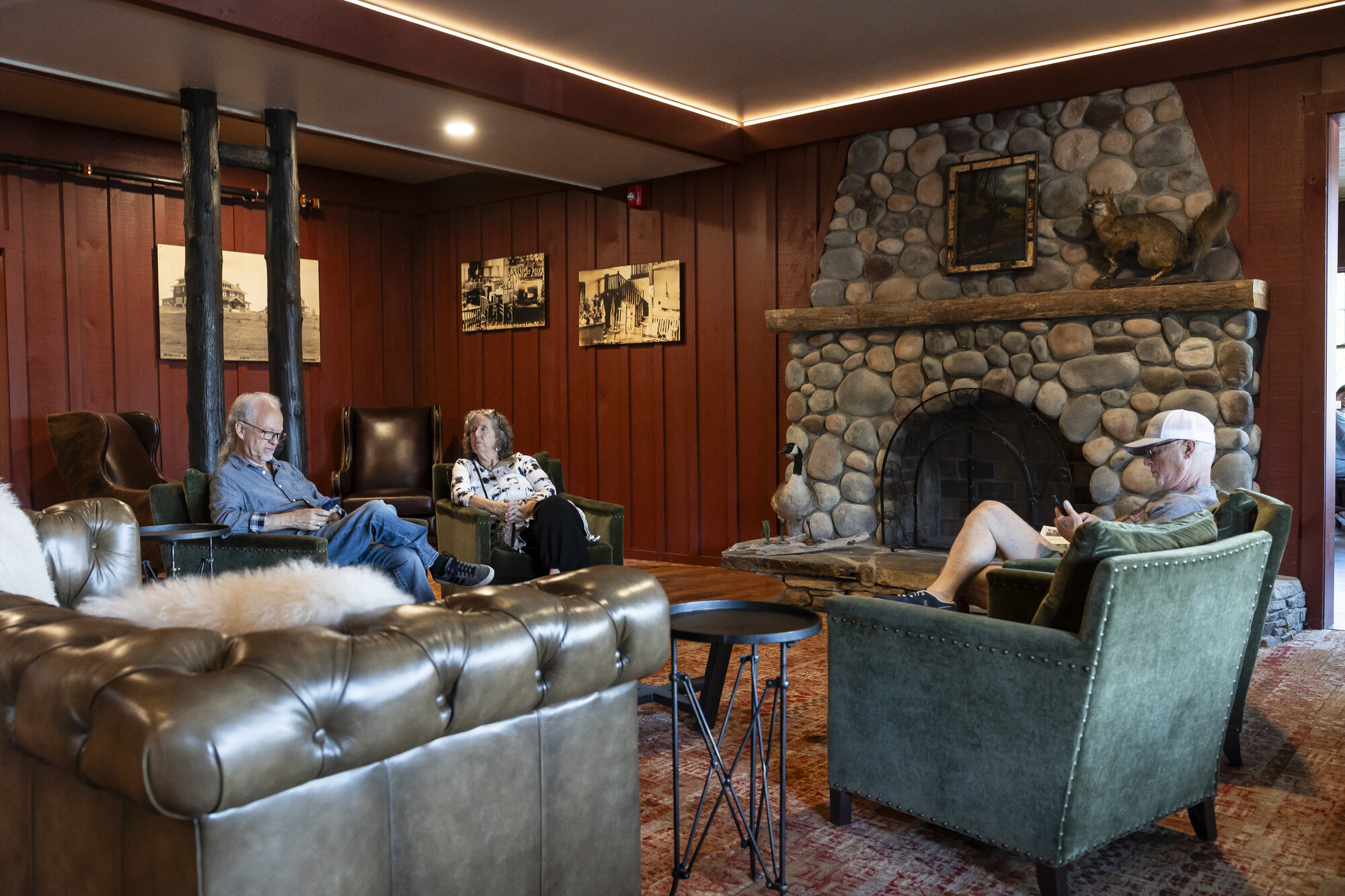A hotel lounge with dark wood walls, large stone fireplace, and people sitting in plush leather couches.