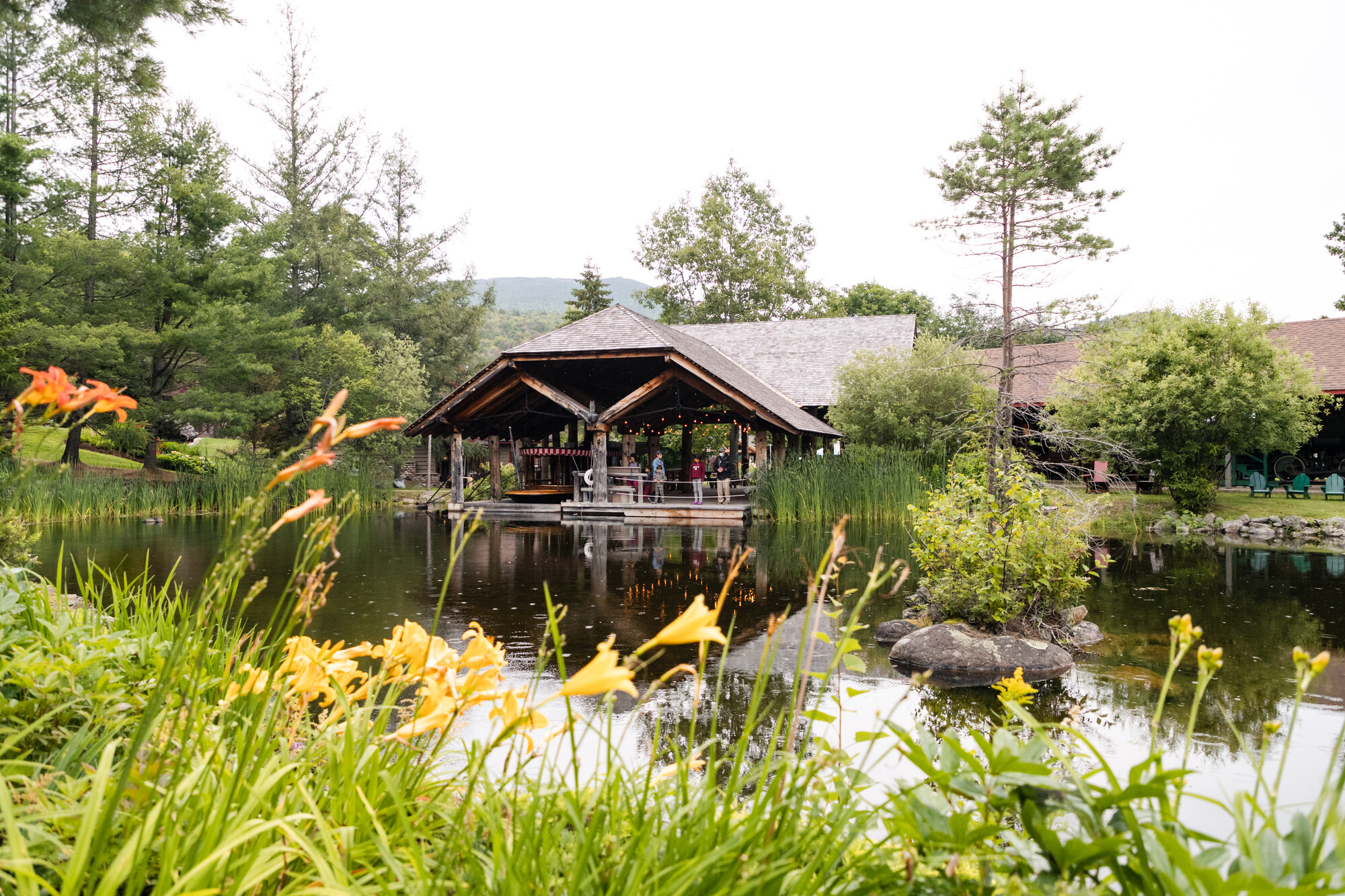 people congregate on the back porch of a building that connects to a pond. 