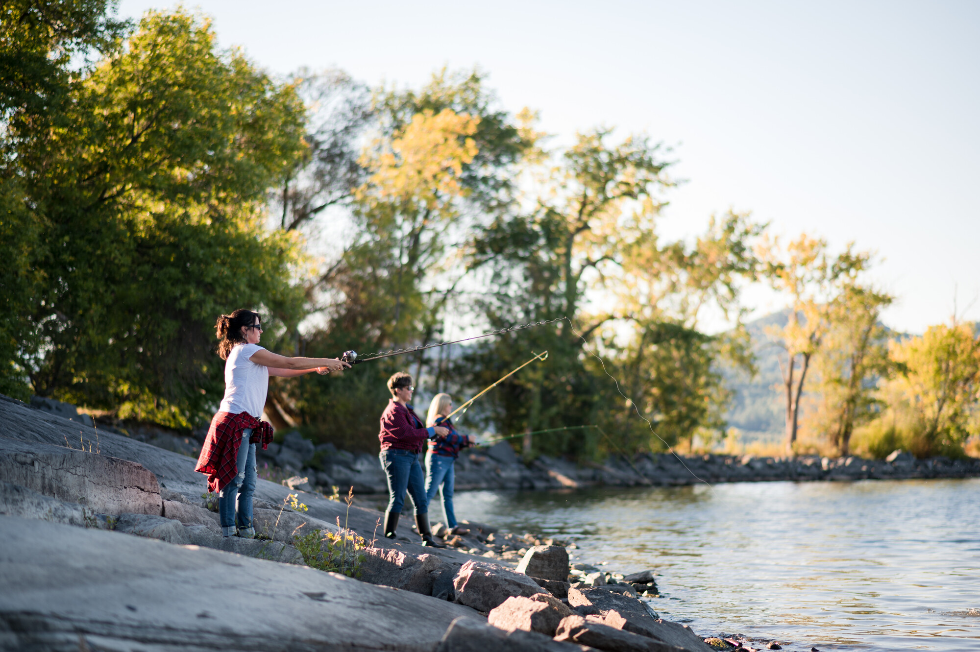 Three women fish from a rocky shore.