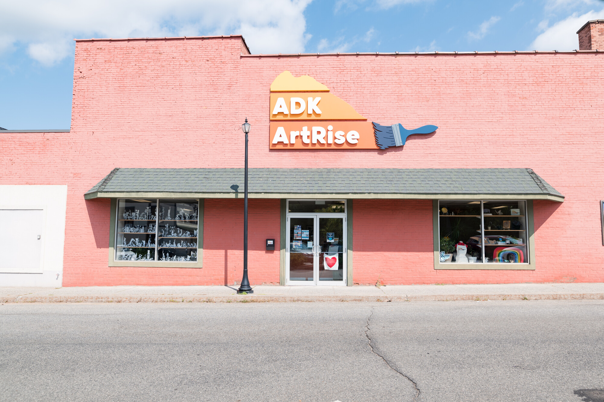 A brick building with sign that includes a paintbrush and the ADK ArtRise ogo.