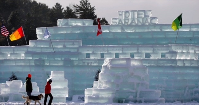 Two people walk by a castle made of ice in winter.