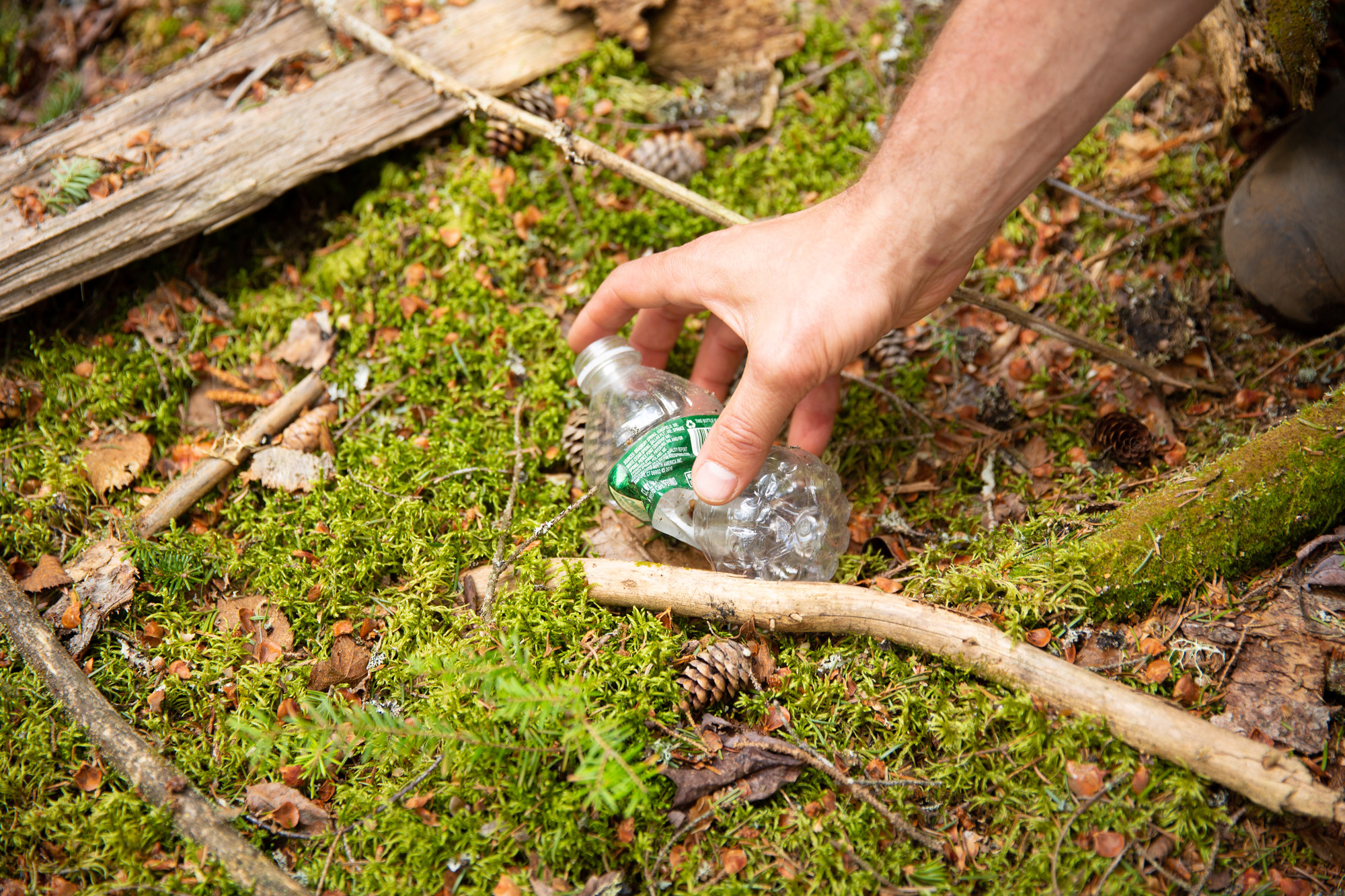 A human picking up a plastic water bottle thrown on the ground.