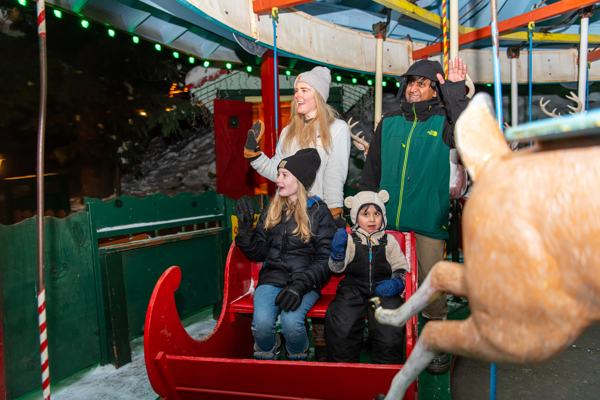 A family rides a brightly lit Christmas carousel. 