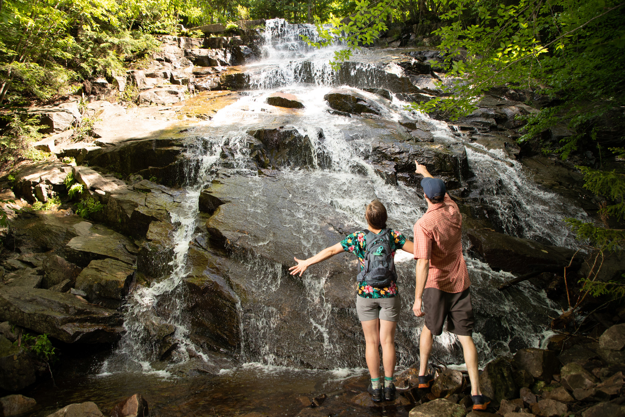 Two hikers stand at the base of a waterfall.