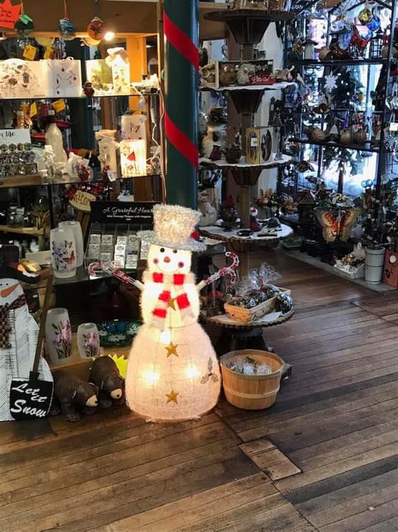 A jaunty, lit snowman Christmas ornament stands in front of shelves stocked with Christmas decor.