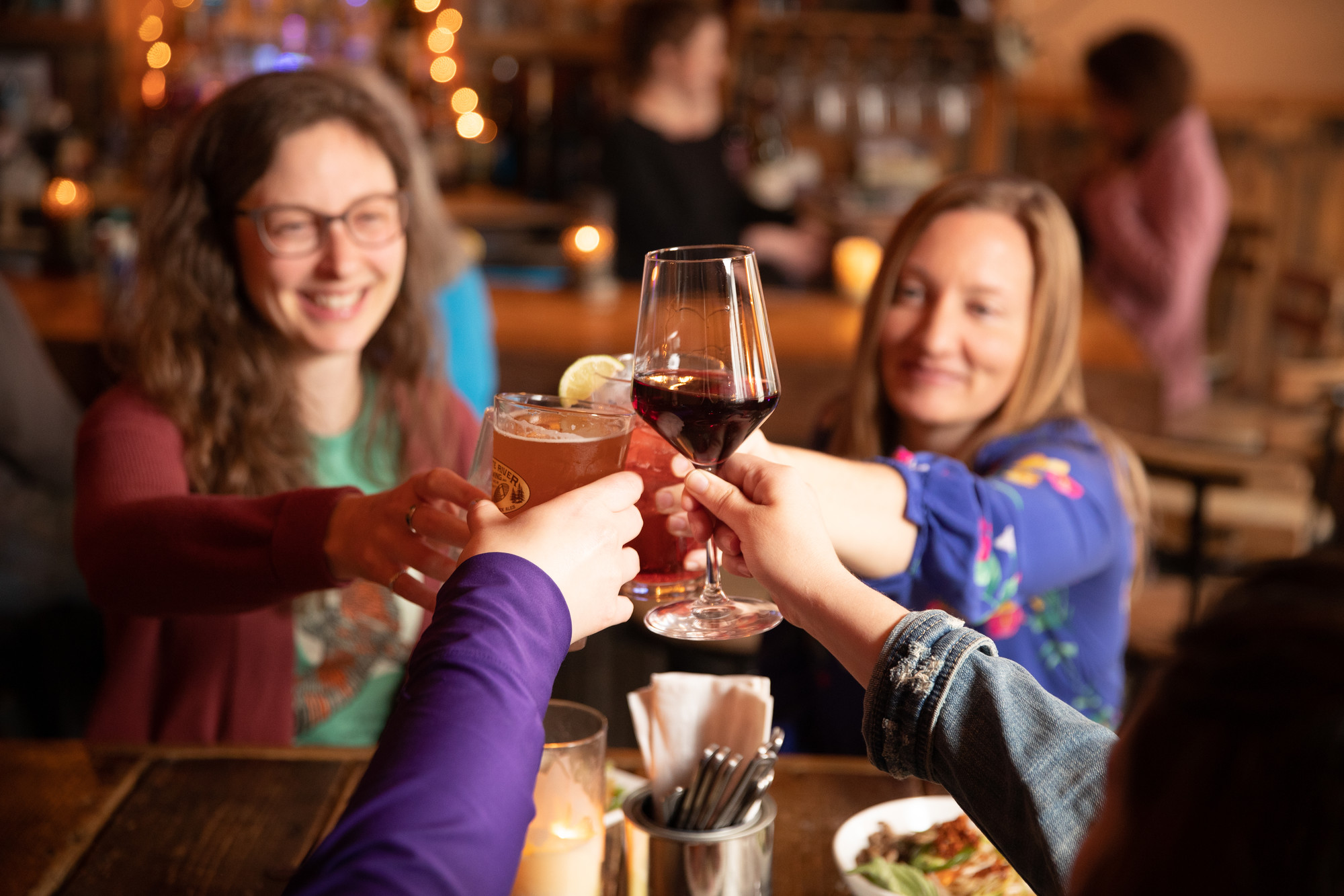 A group of people, including two women, toast glasses over a restaurant table.