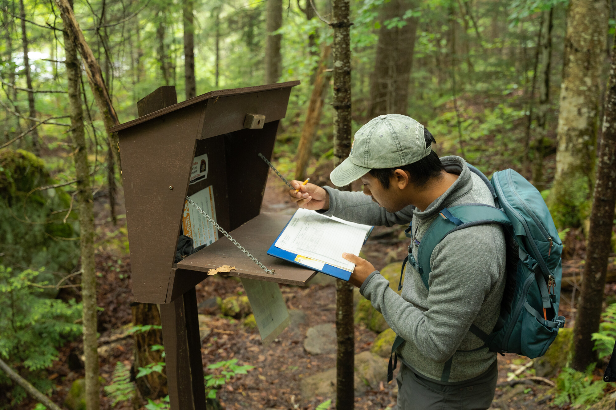 Person wearing hat and backpack signs in at trailhead
