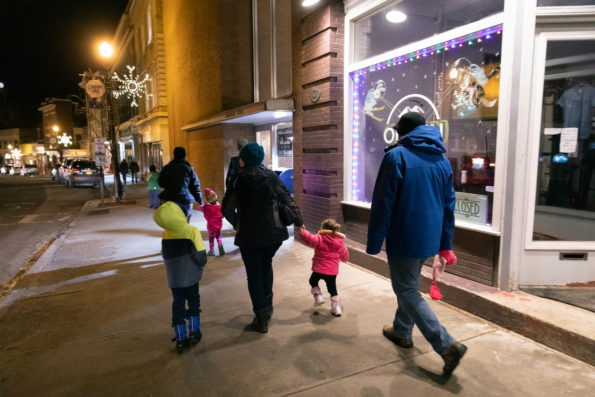 A family walks down a sidewalk with shops in winter. 