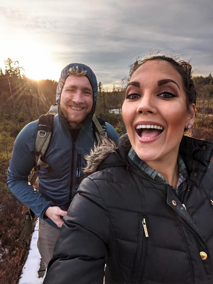 Two people walk along a boardwalk through the woods.