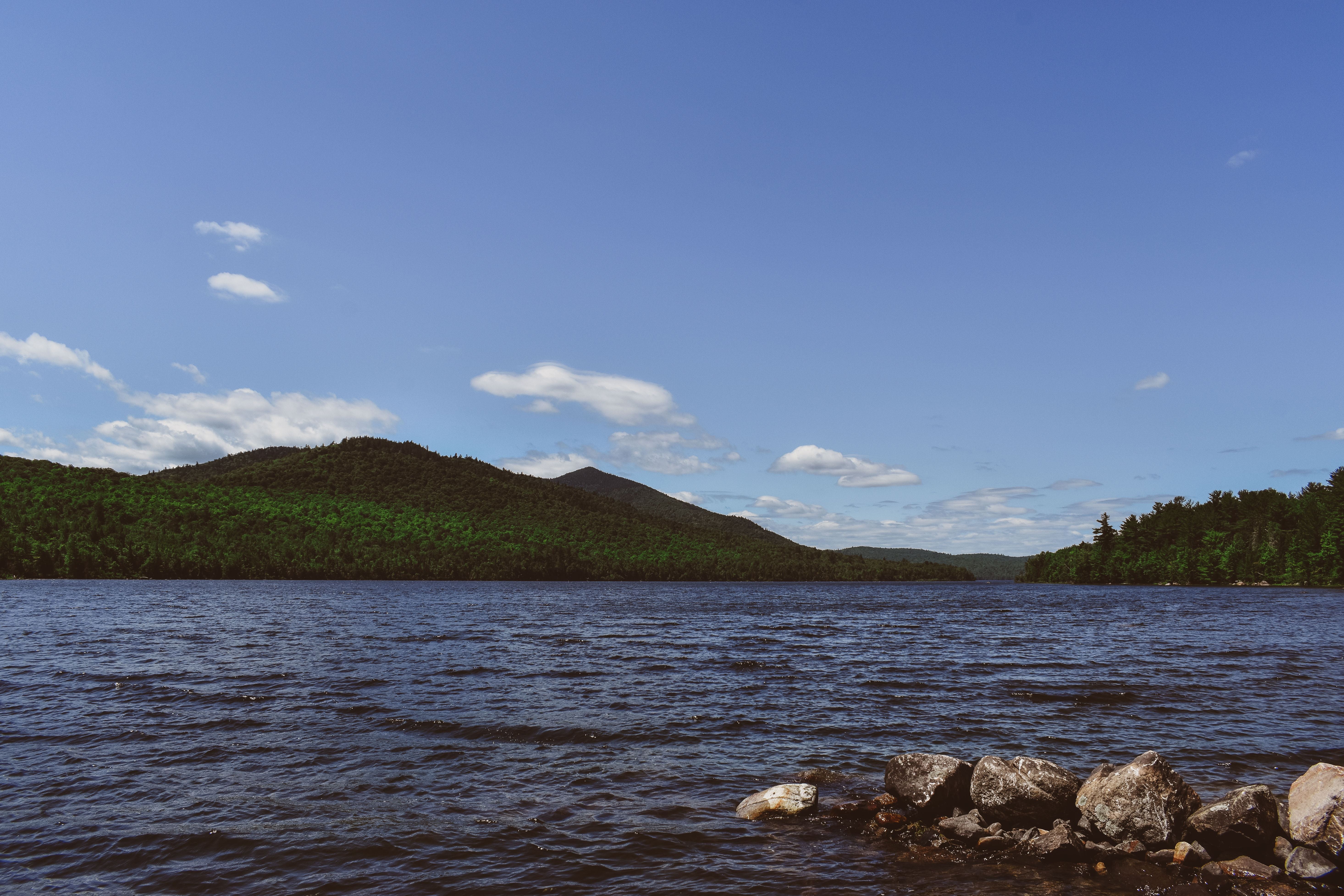 A scenic view of Taylor Pond with deep blue water, light blue sky, a few clouds, and rolling hills.