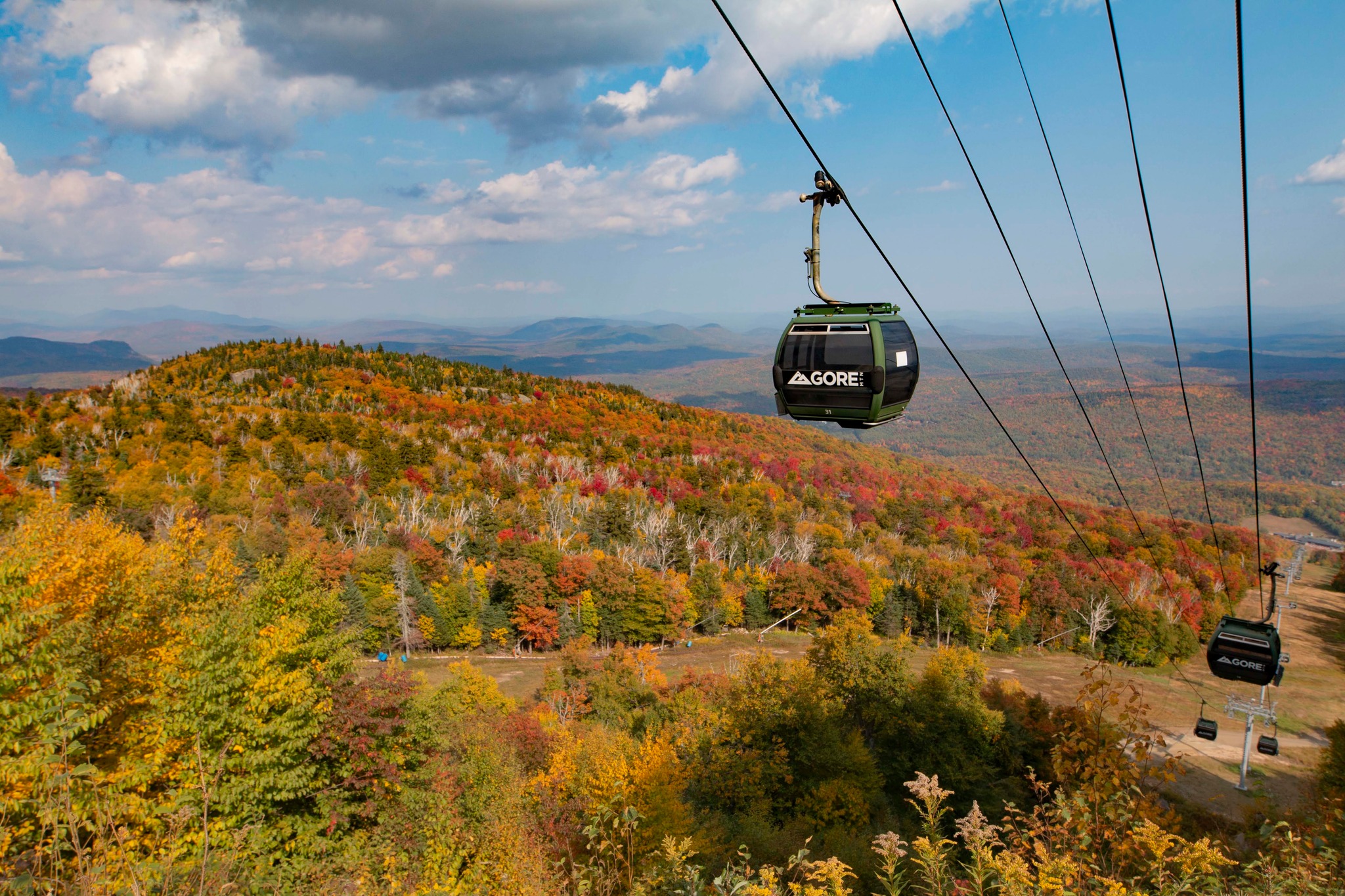 Gondolas in operation at Gore Mountain in the fall, with a backdrop of mountains adorned in seasonal fall foliage 