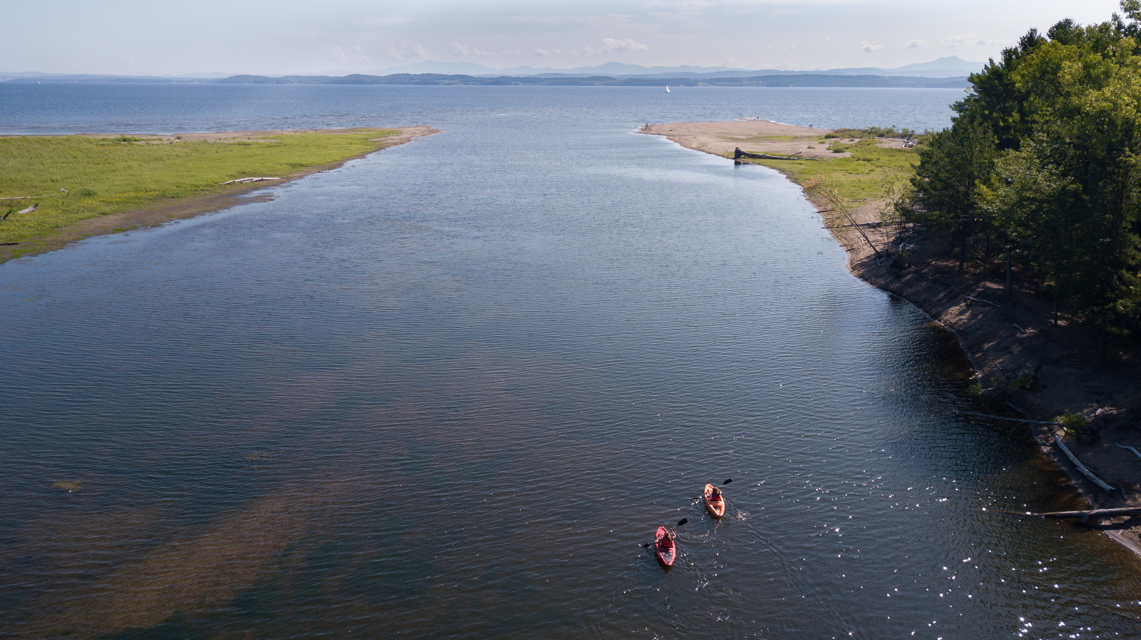 Two kayakers heading out into the big lake from a river.