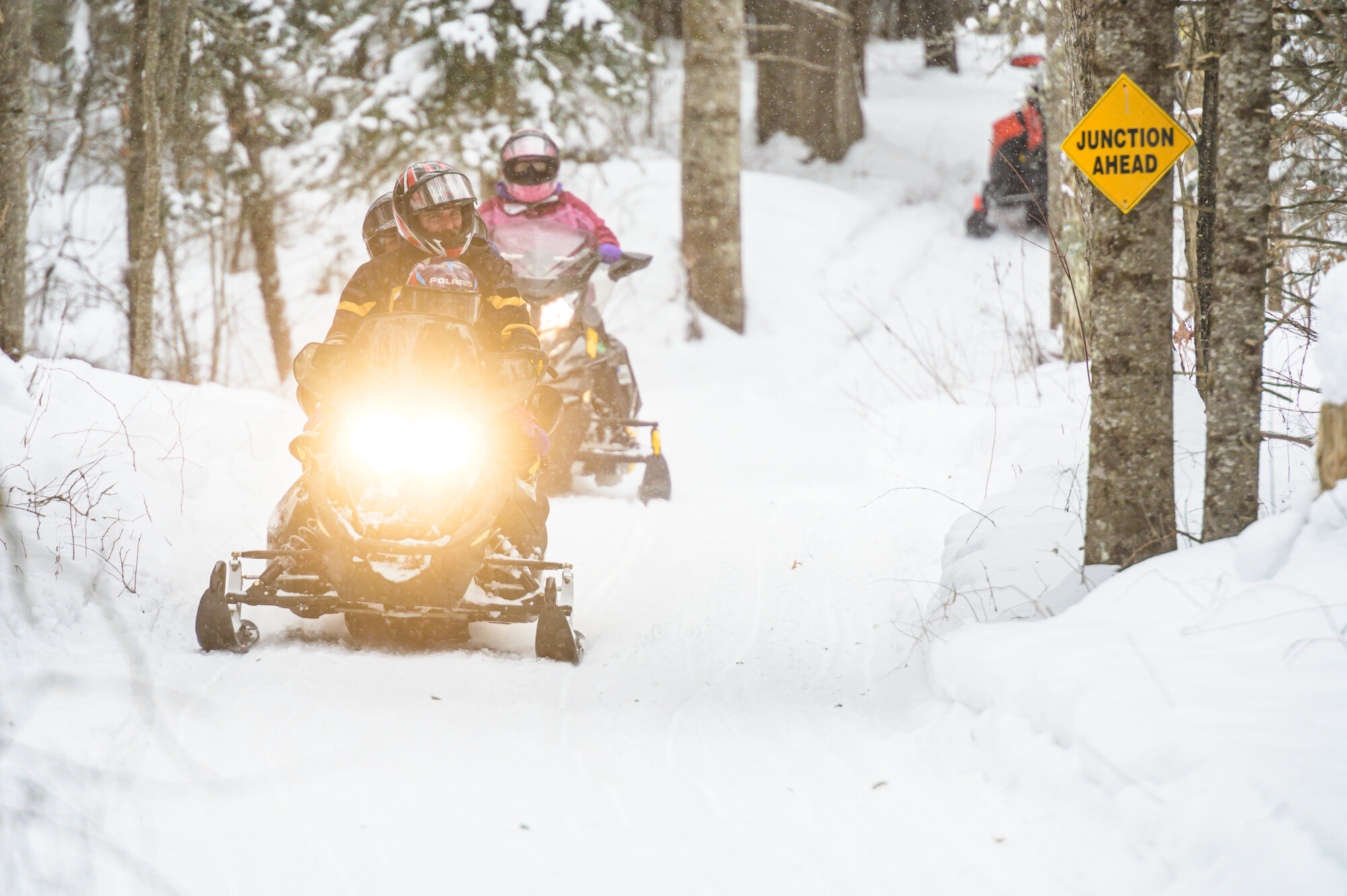 four people snowmobile on a snowy trail.