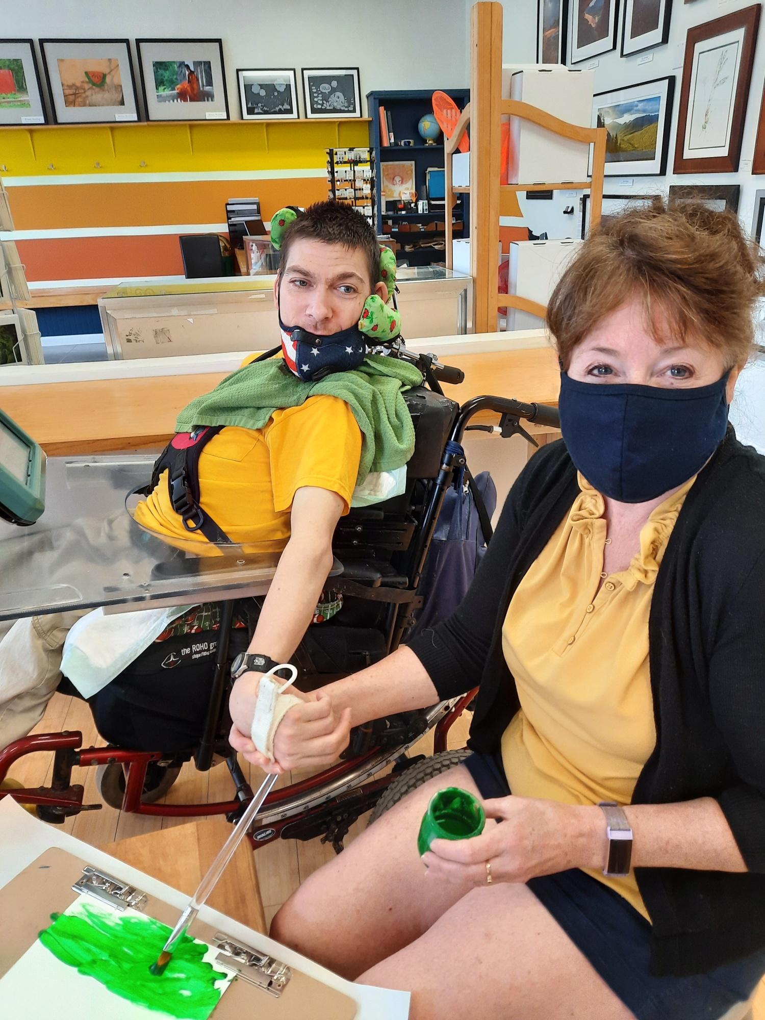A young man in a wheel chair paints with the assistance of his aide, Renee Clark, the mother of Brittany Sternberg.