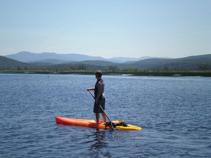 A man paddles on a standup paddleboard with mountains in the background