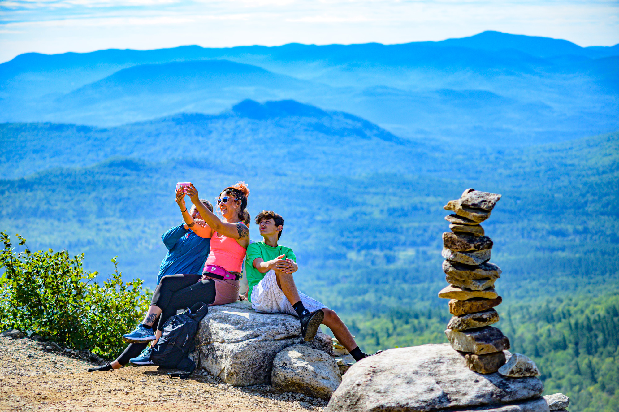 A mom poses with her two young sons for a selfie at the peak of a mountain.