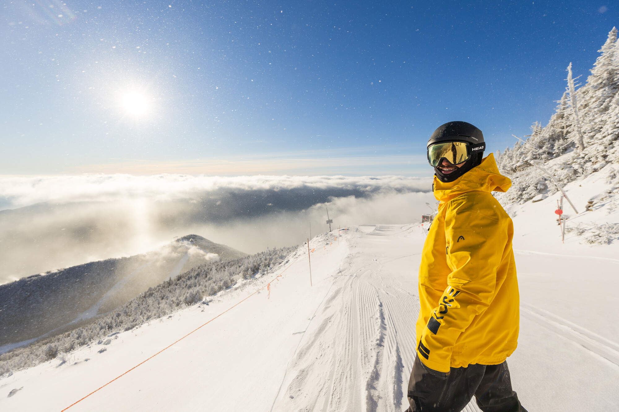 A snowboarder smiling for the camera at the summit of Whiteface Mountain.