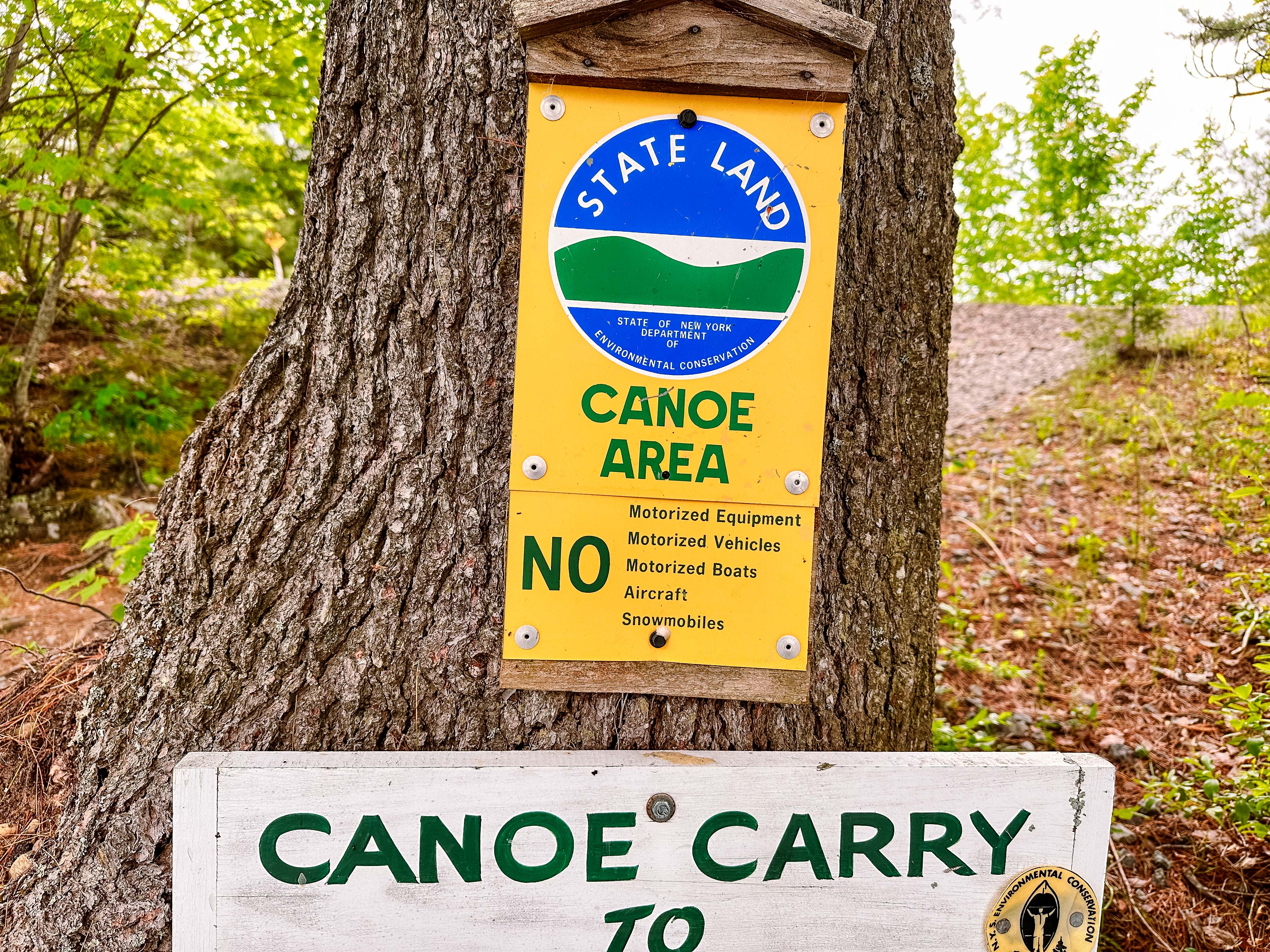 A state land sign nailed to a tree marking the boundary into the Canoe Area, with a canoe carry sign below it