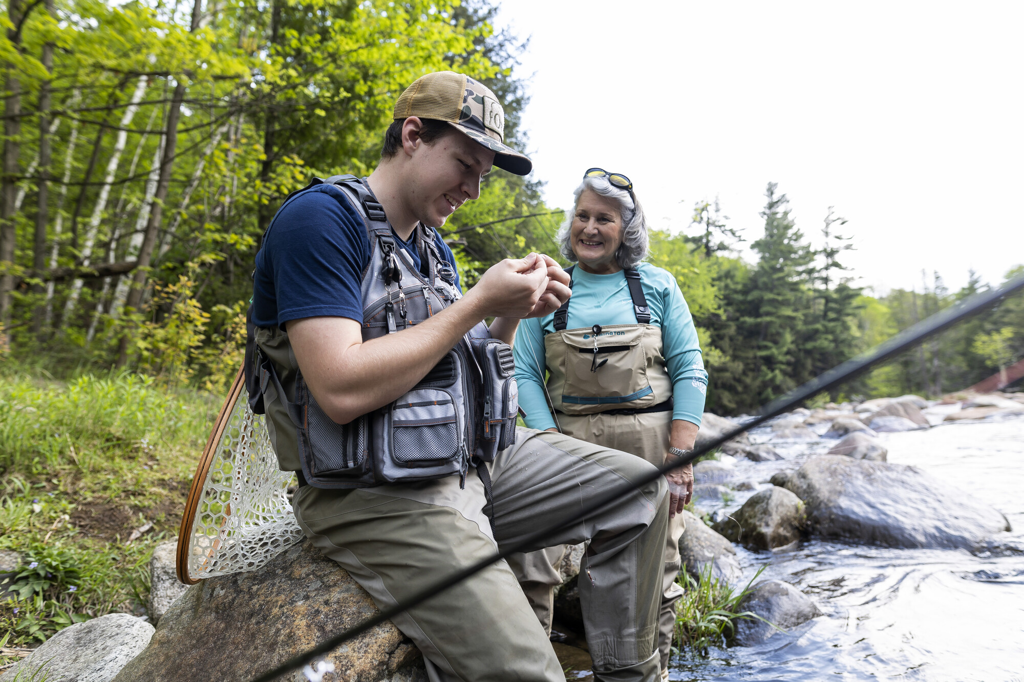 A woman helps another angler tie a fly on.
