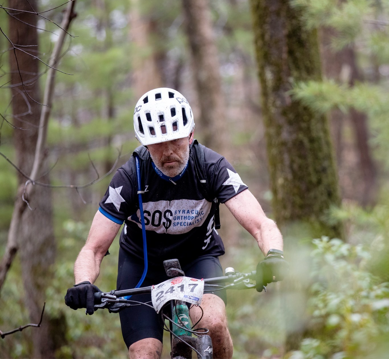 A man covered in mud bikes uphill.