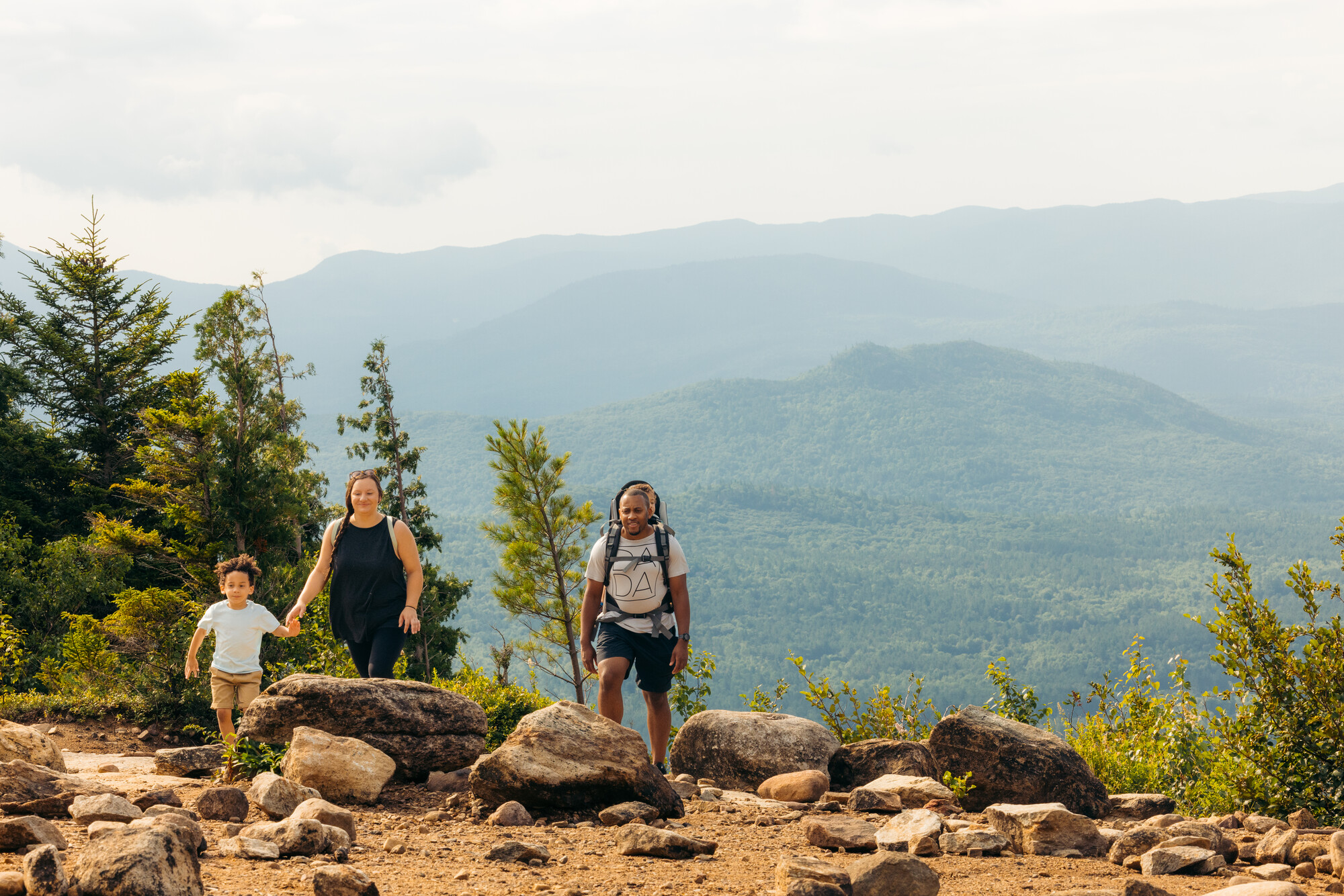 Family of four walks along summit with mountain view in background
