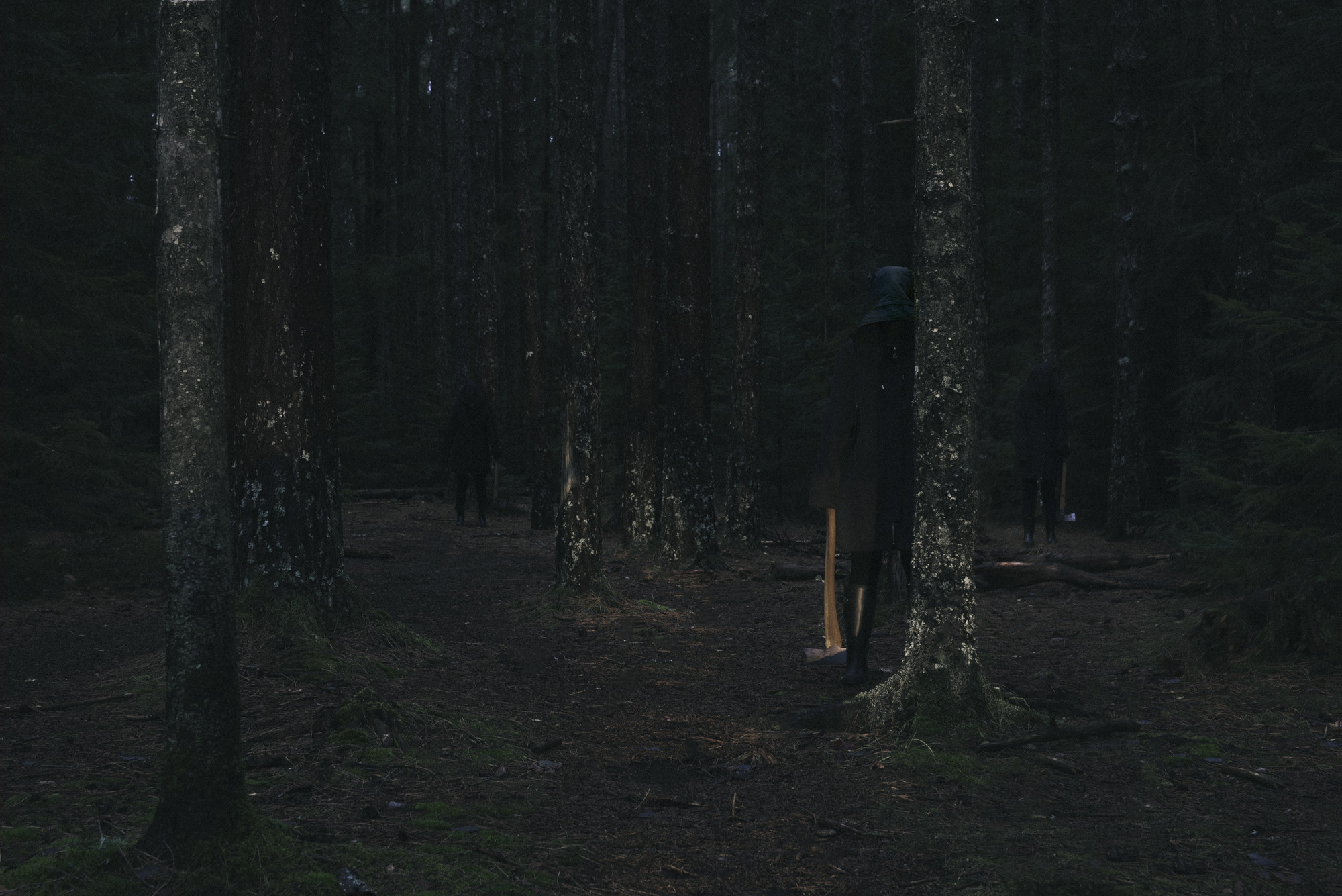 Hooded figures hold axes in the woods