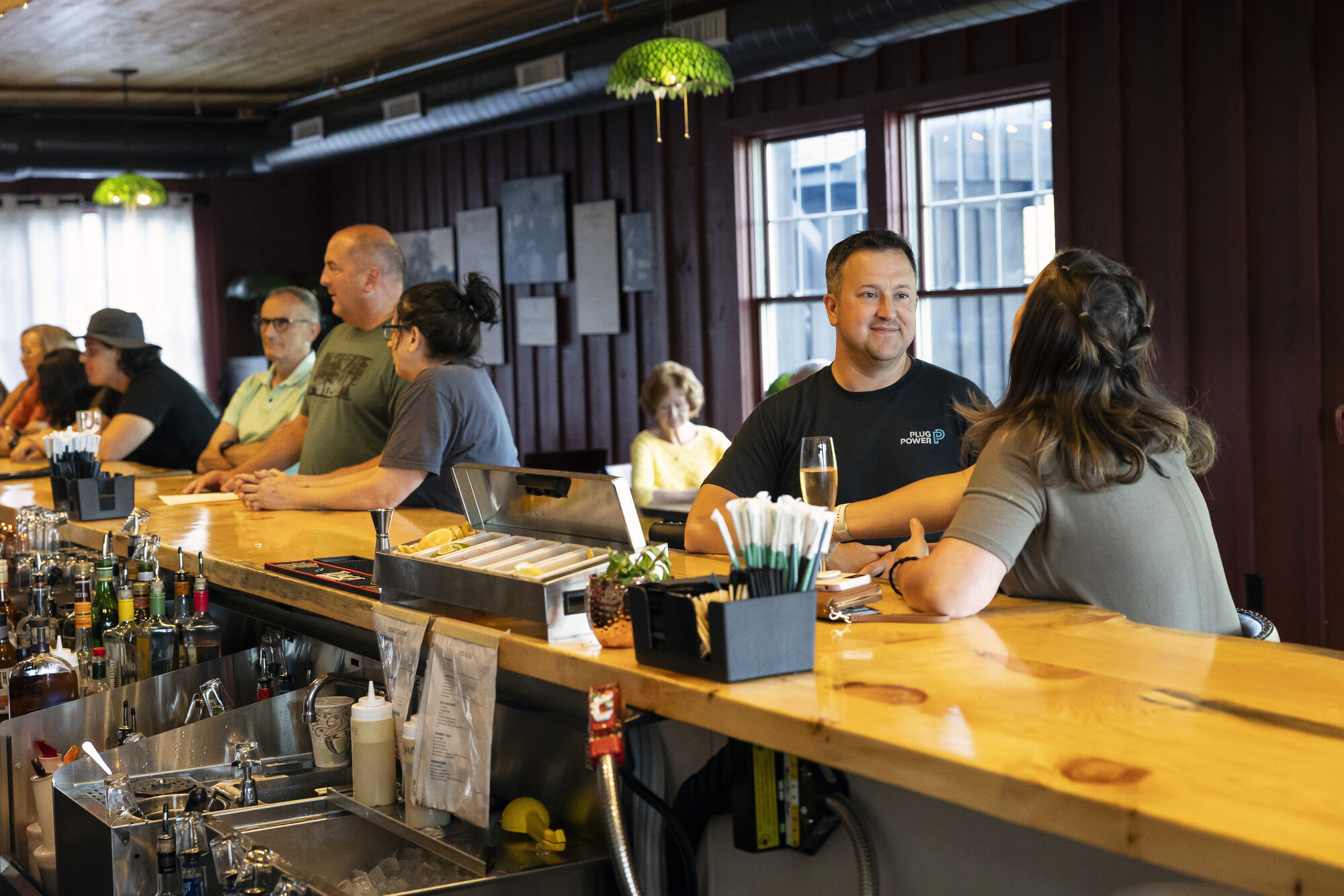 Adults sit at a wood bartop in a cozy restaurant.
