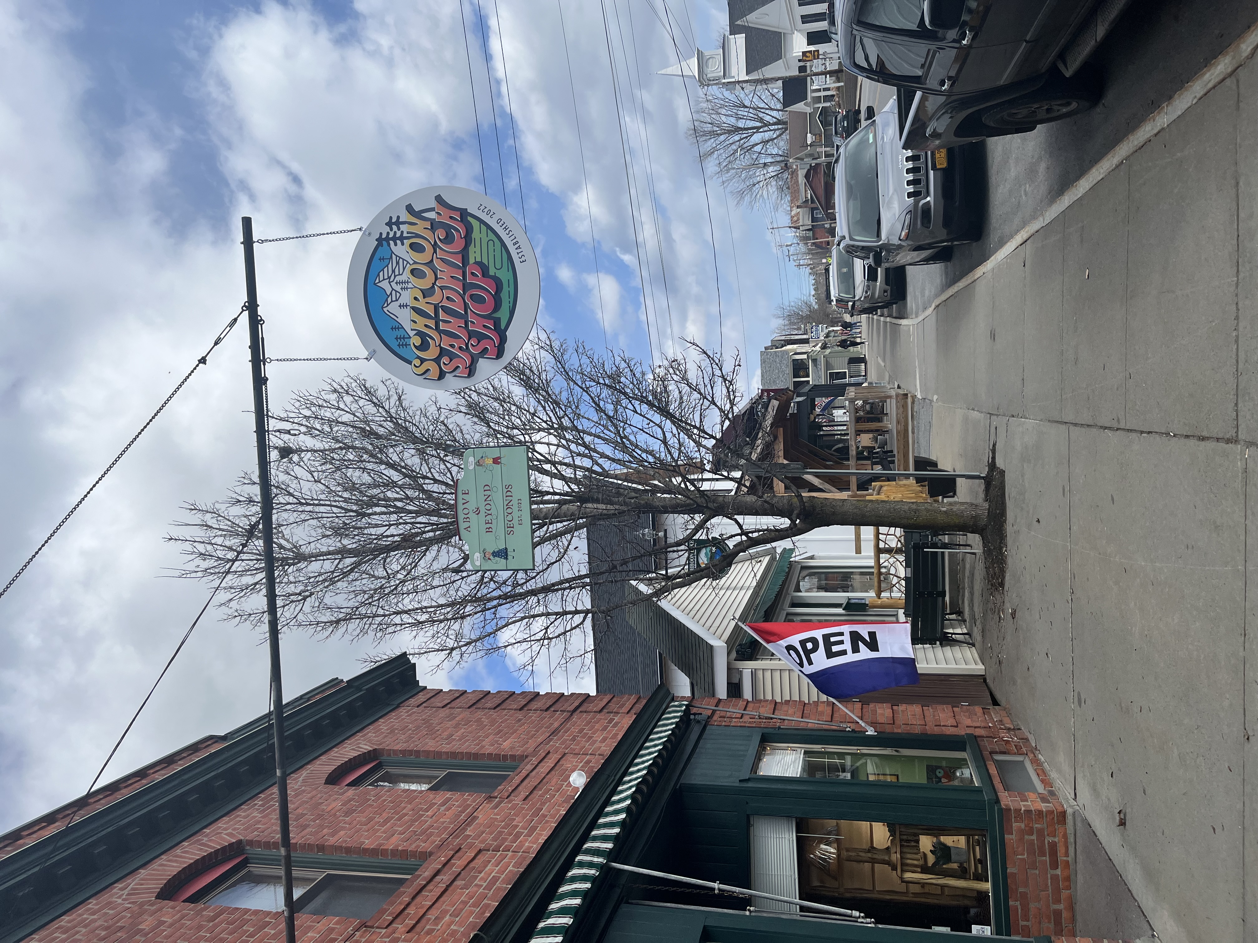 Schroon Lake Sandwich Shop sign hangs in front of a brick building on a small-town Main Street.