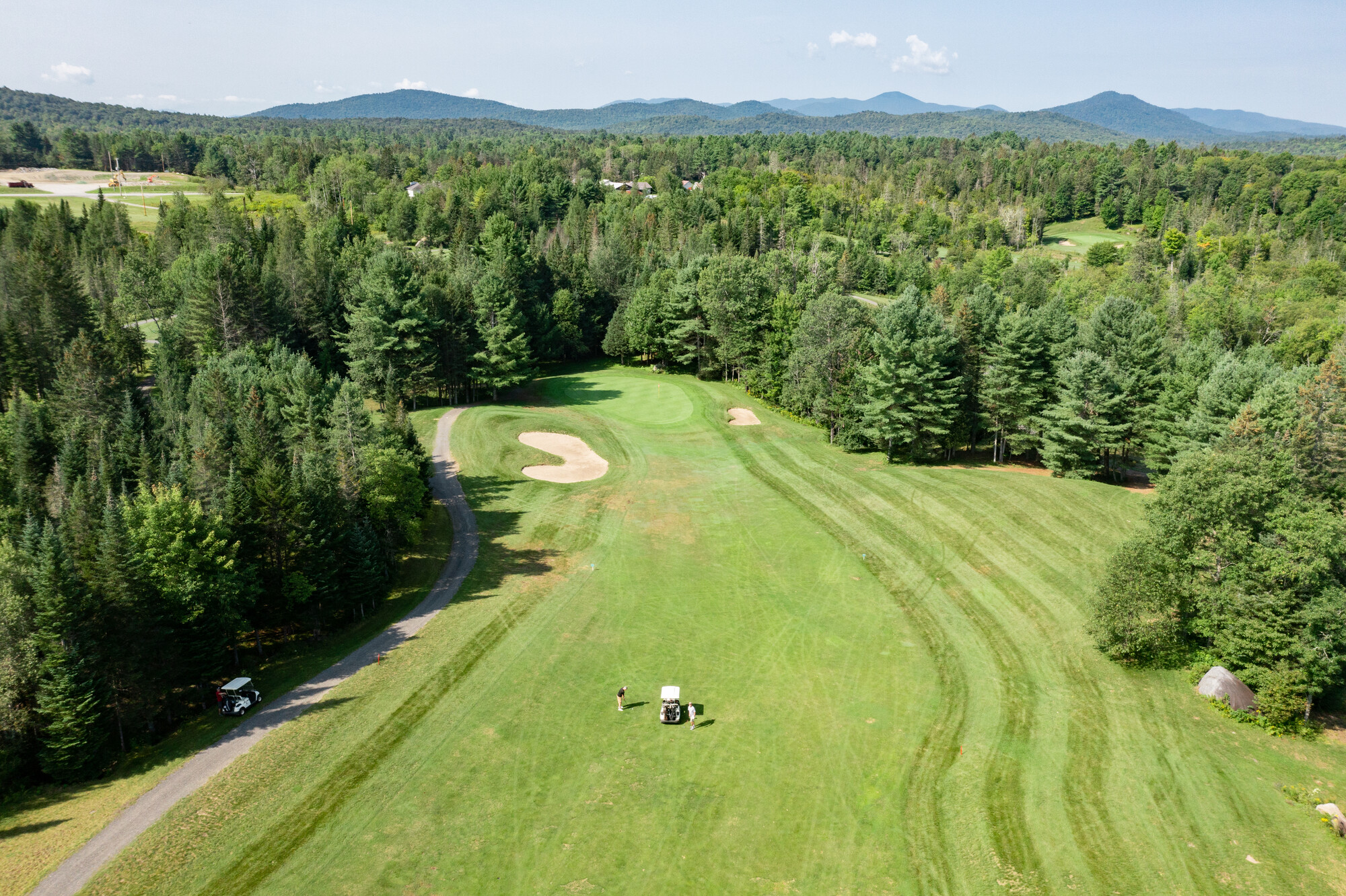 An aerial view of the High Peaks Golf Course with a fairway, rough, and sand trap, and people playing a hole.