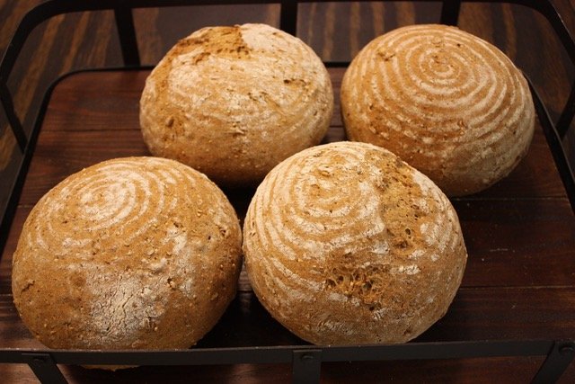 Four round, rustic loaves of bread in a wood and metal shopping basket.