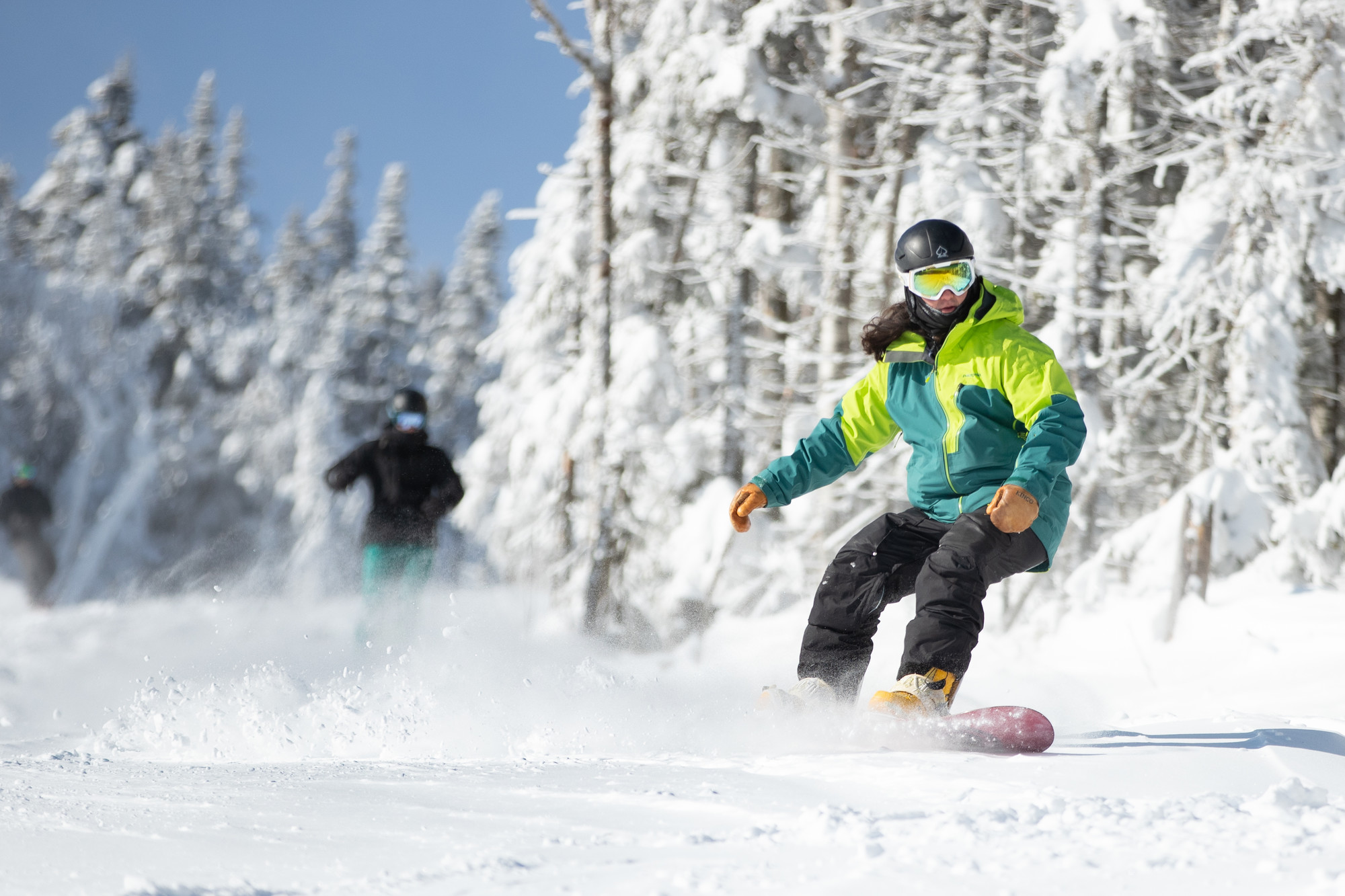 A snowboarder and skier race through powdery snow.