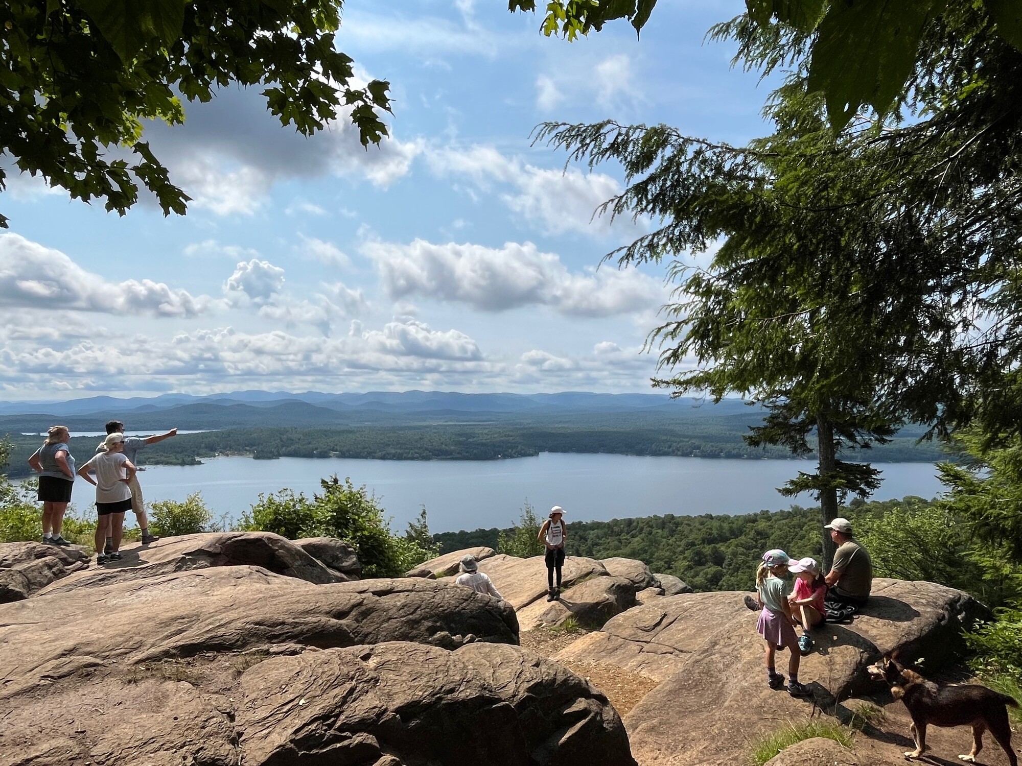 People stand on top of a rocky mountain top overlooking a lake. 