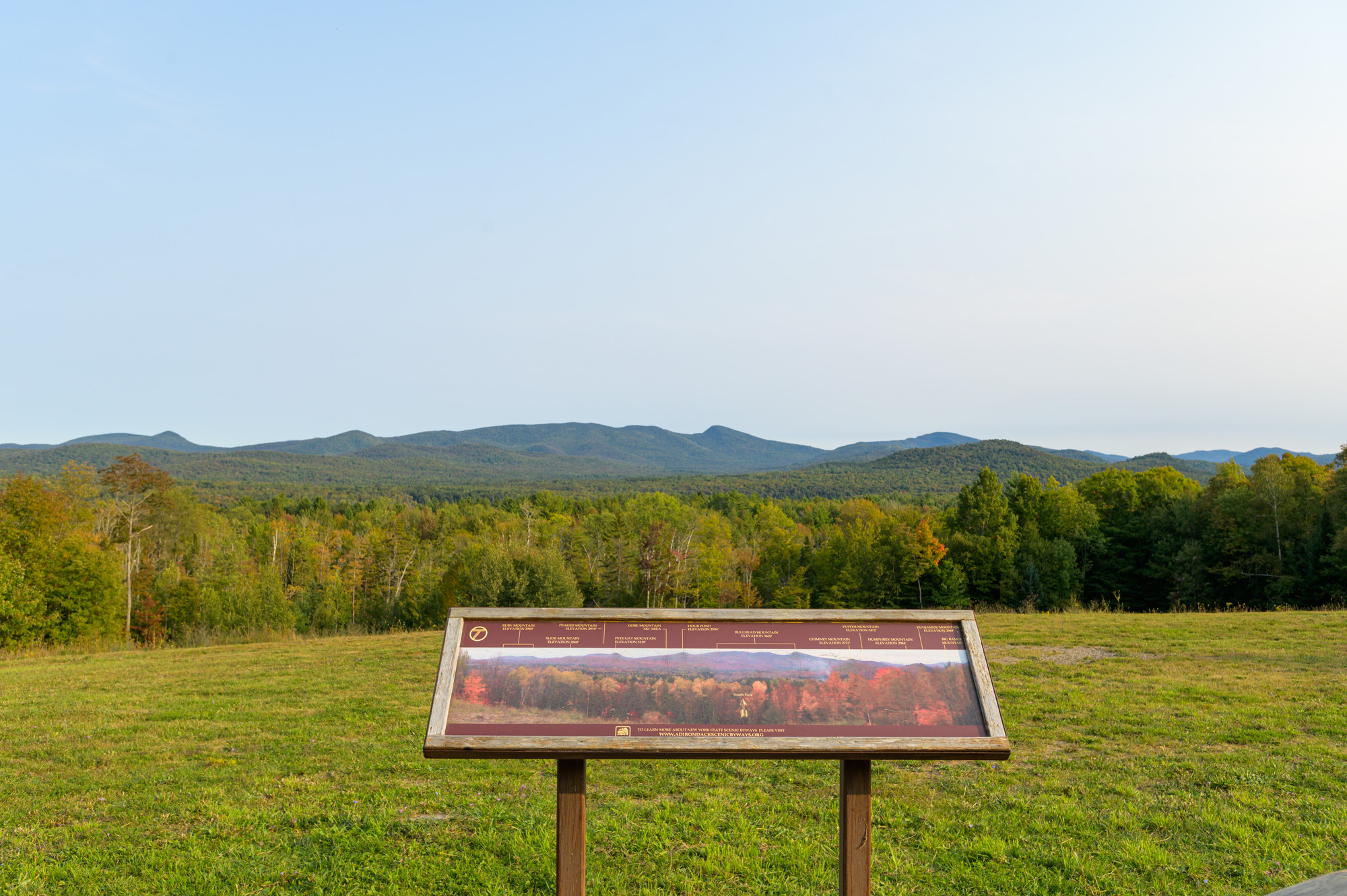 A scenic overlook with mountains in the distance and a sign identifying features in the foreground.