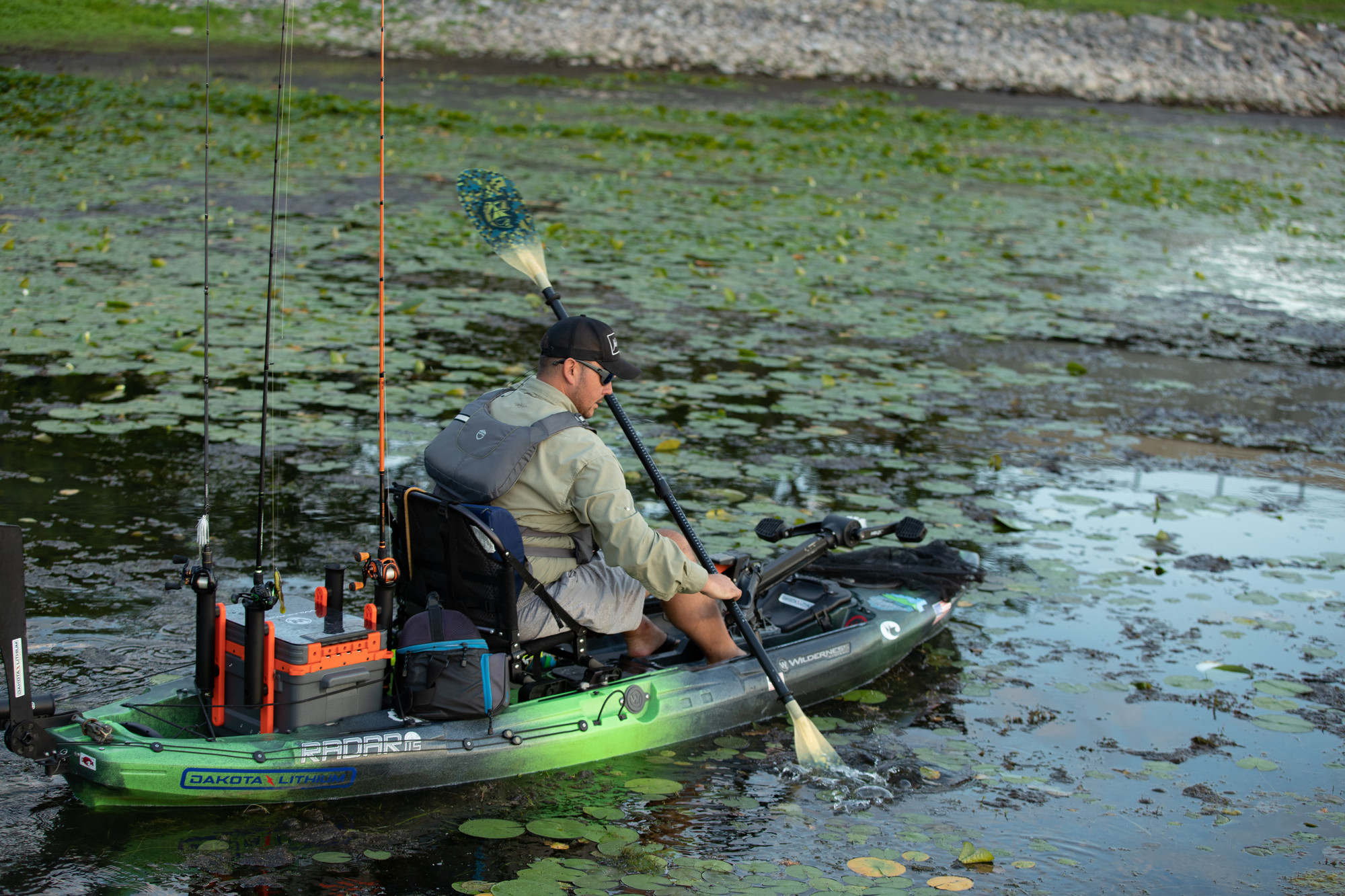 A fisherman kayaking through lily pads on Lake Champlain.