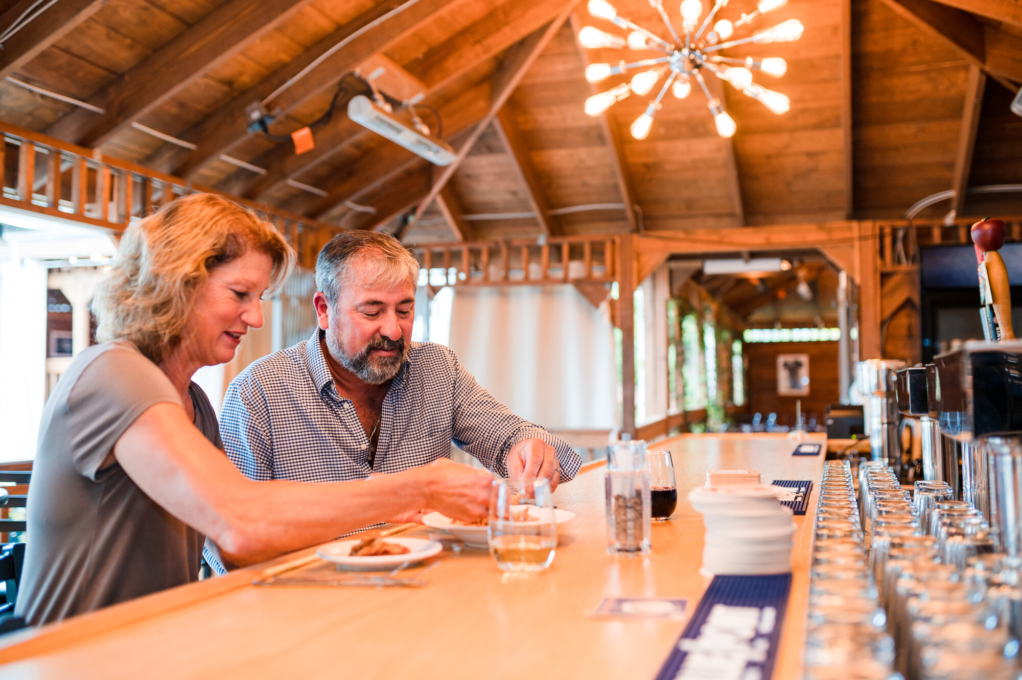 A man and woman sit at a wood bar, drinking cocktails at a rustic wood bar.