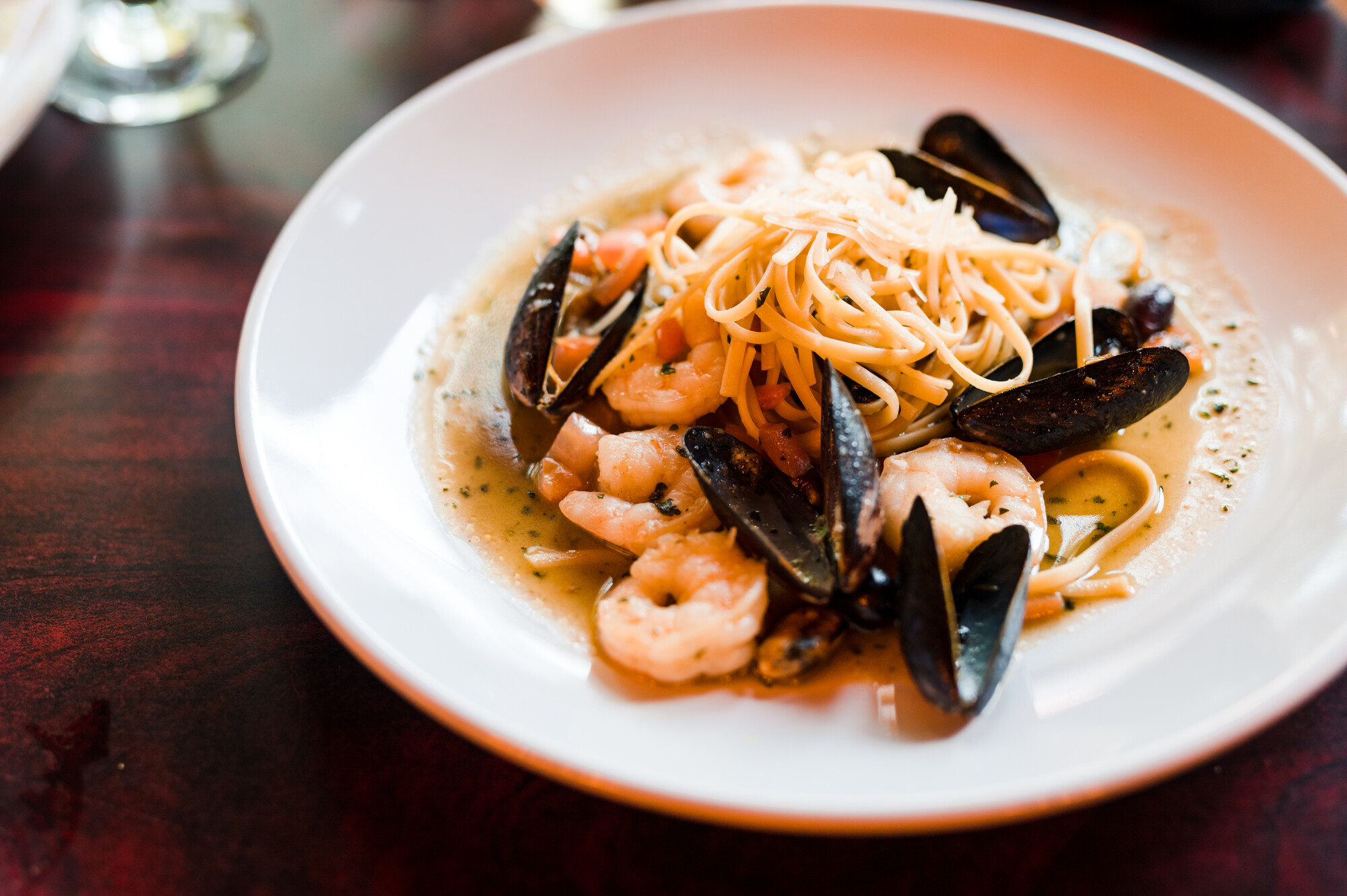 Close-up of mussels and pasta in a shallow white bowl on a wood backdrop.