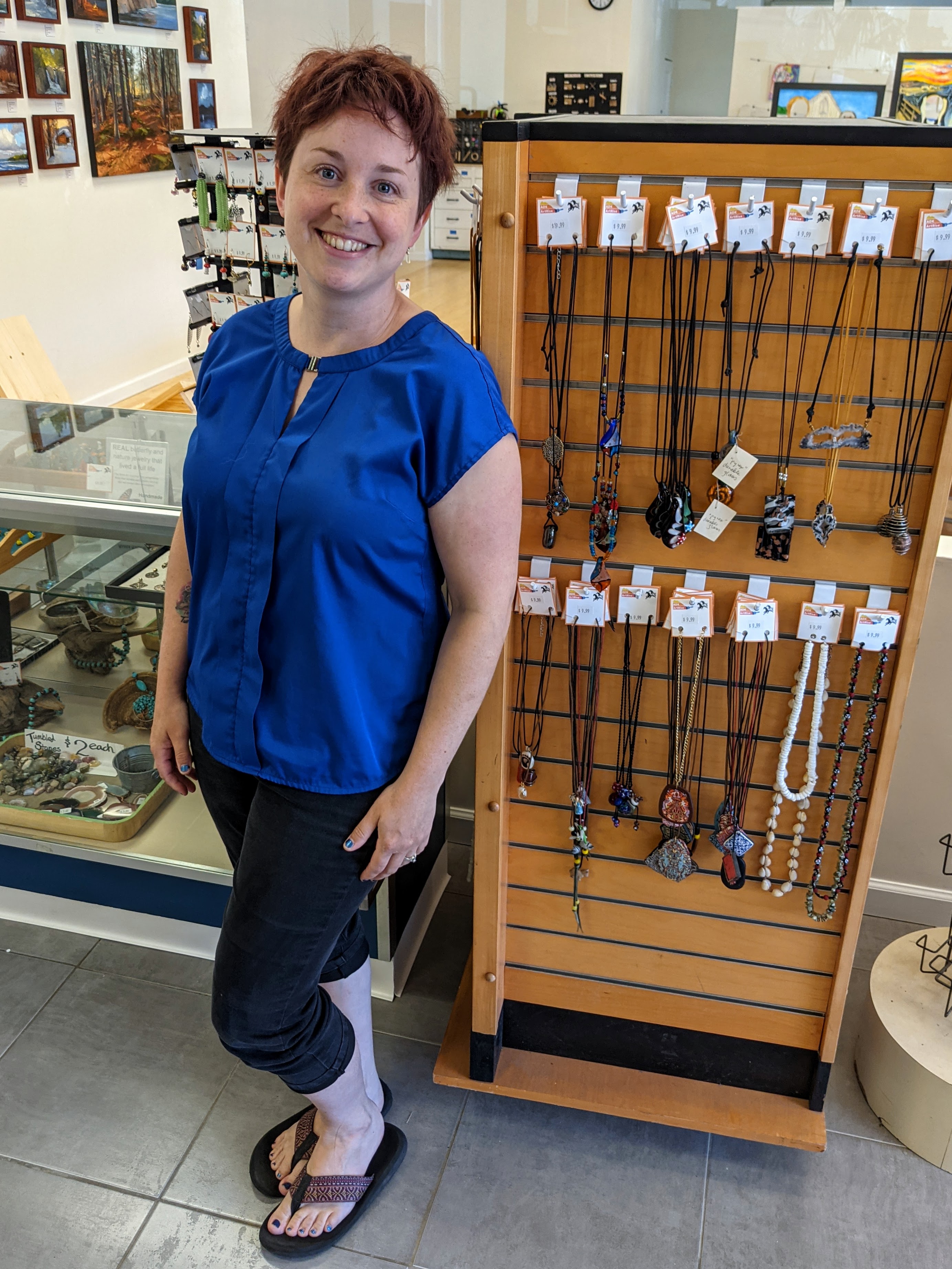 A woman smiles next to a jewelry stand