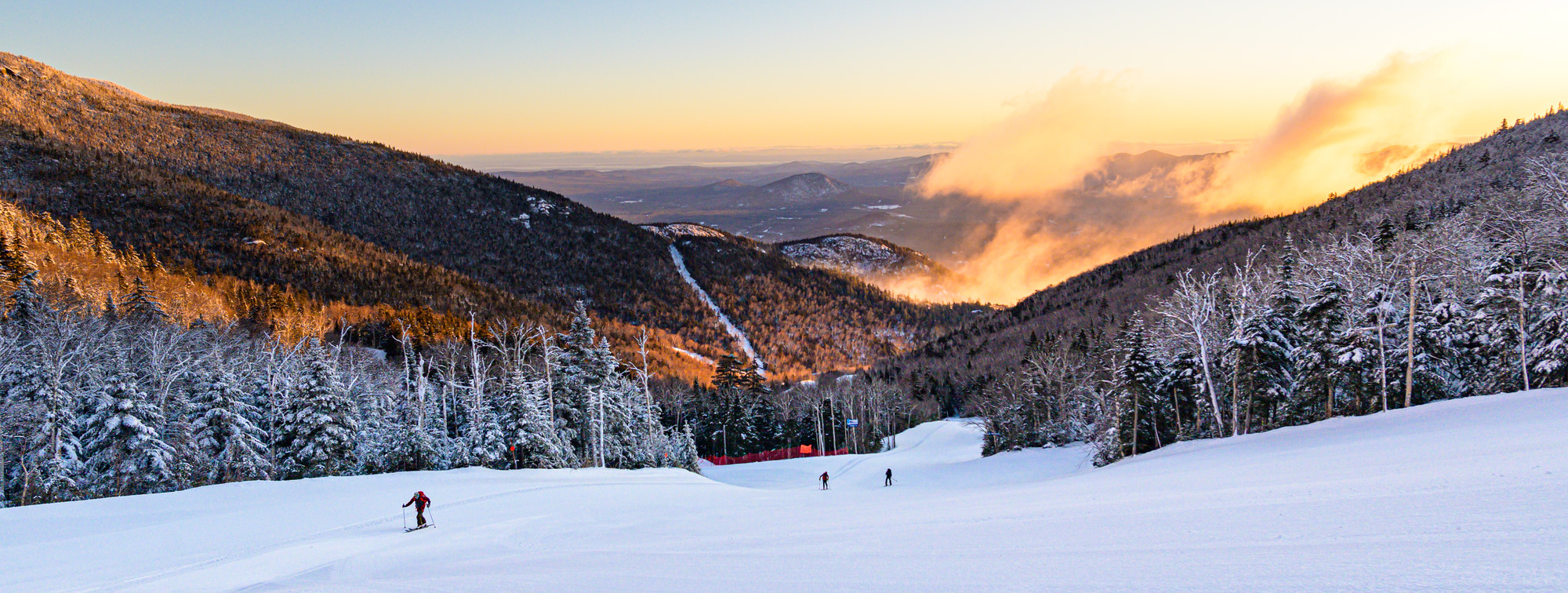 Skiers ski down Whiteface Mountain at sunset. 