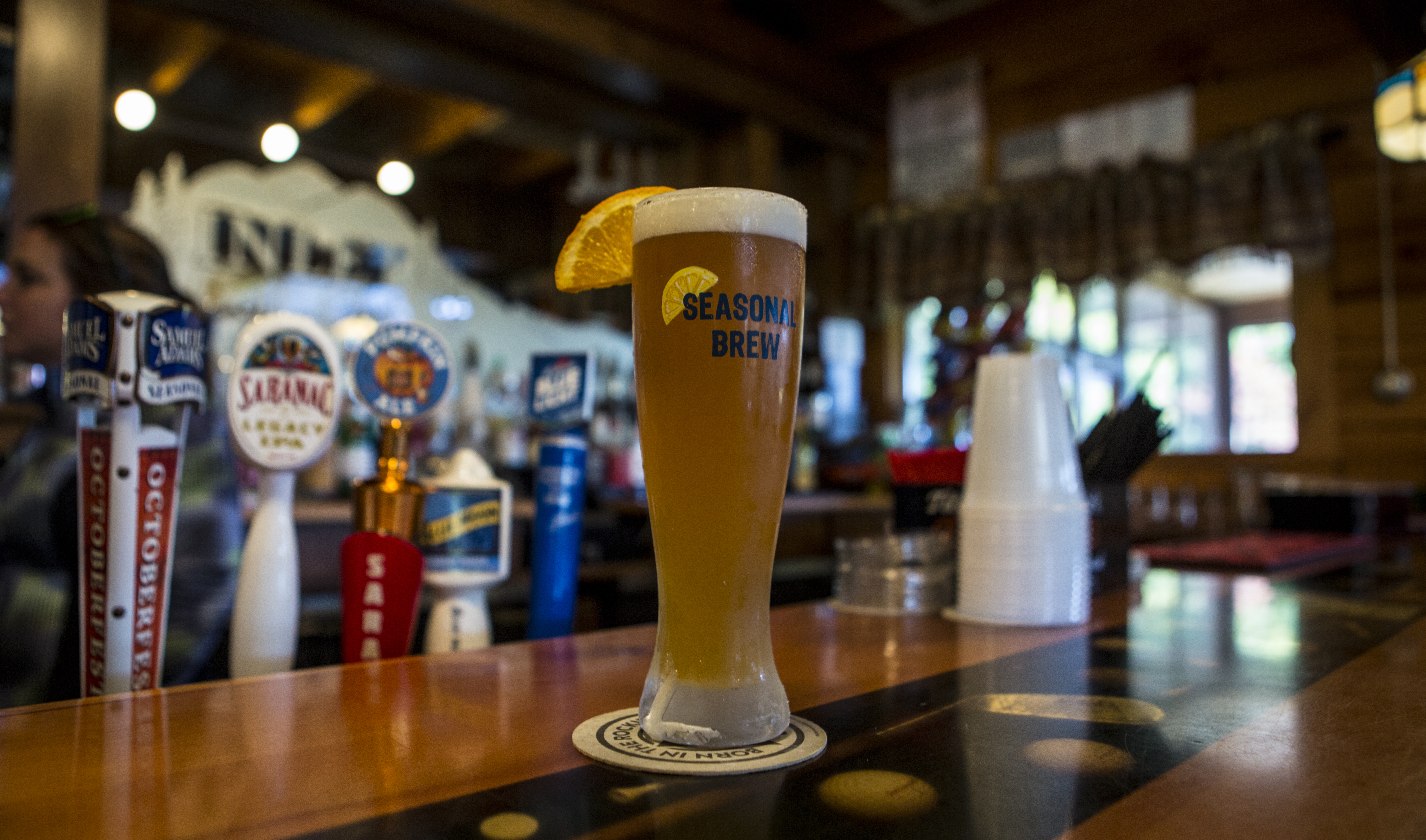 A cold, tall glass of beer sits on an attractive wood bar.