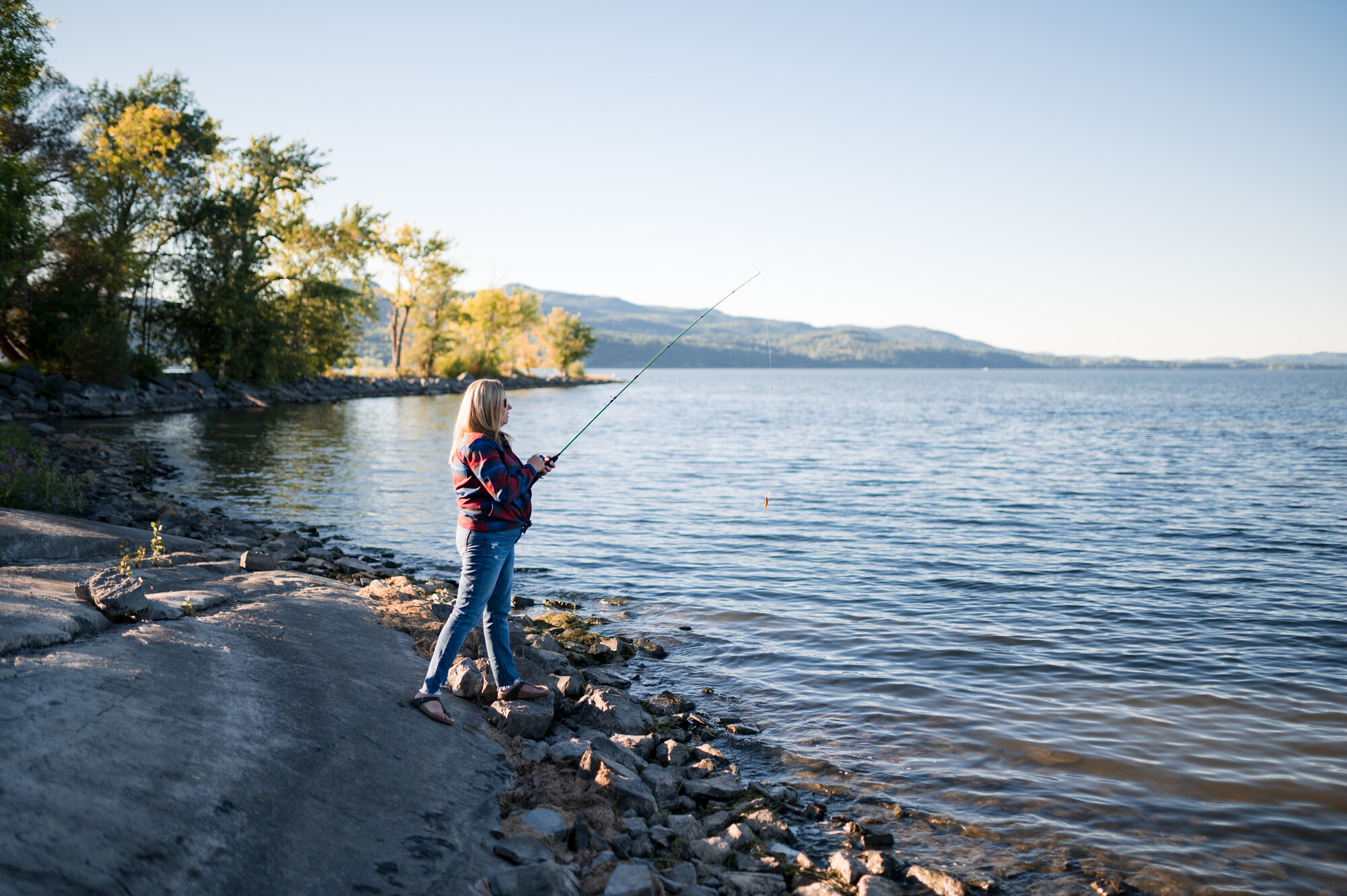 A woman fishes from the shoreline 