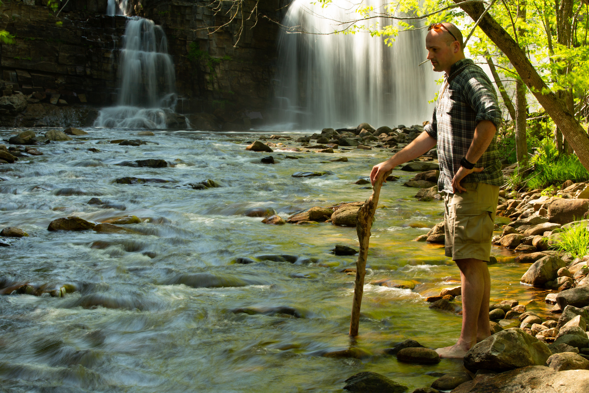 A man with a walking stick in front of a waterfall