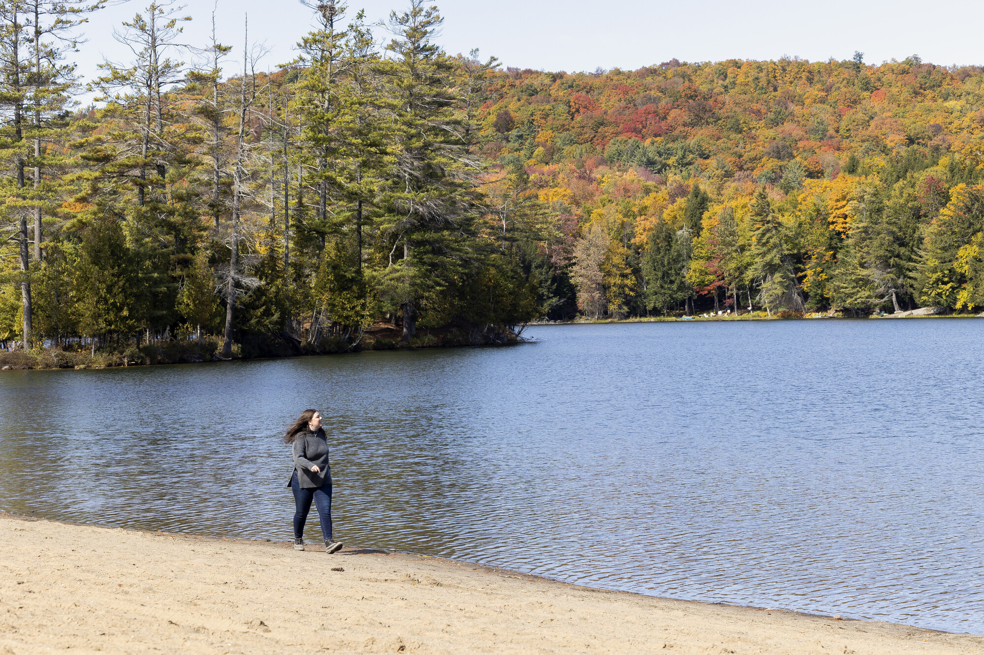 A hiker in motin on the sand of Donnelly beach, with a backdrop of autumn color and reflections in the water