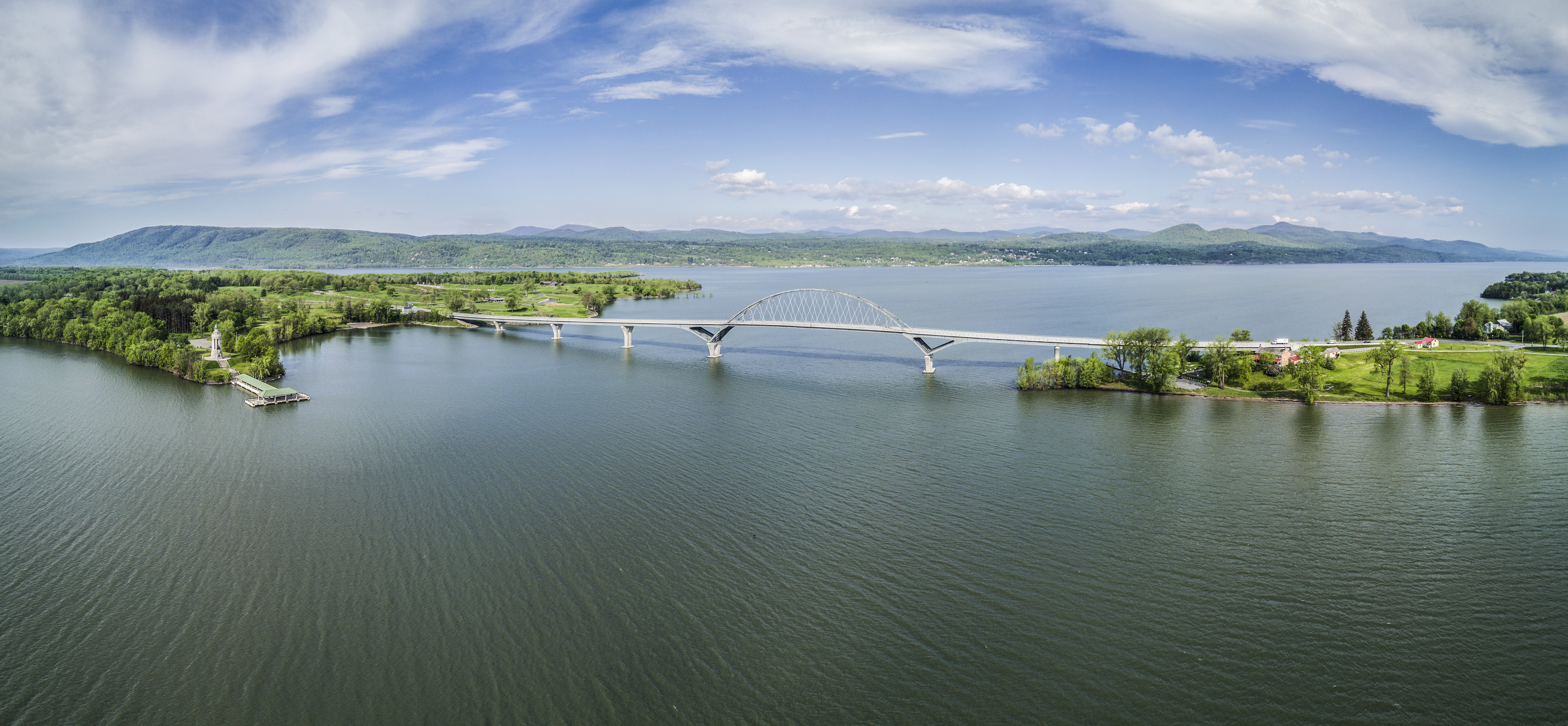 Birds eye view of the Champlain Bridge with lots of open water and distant mountains.