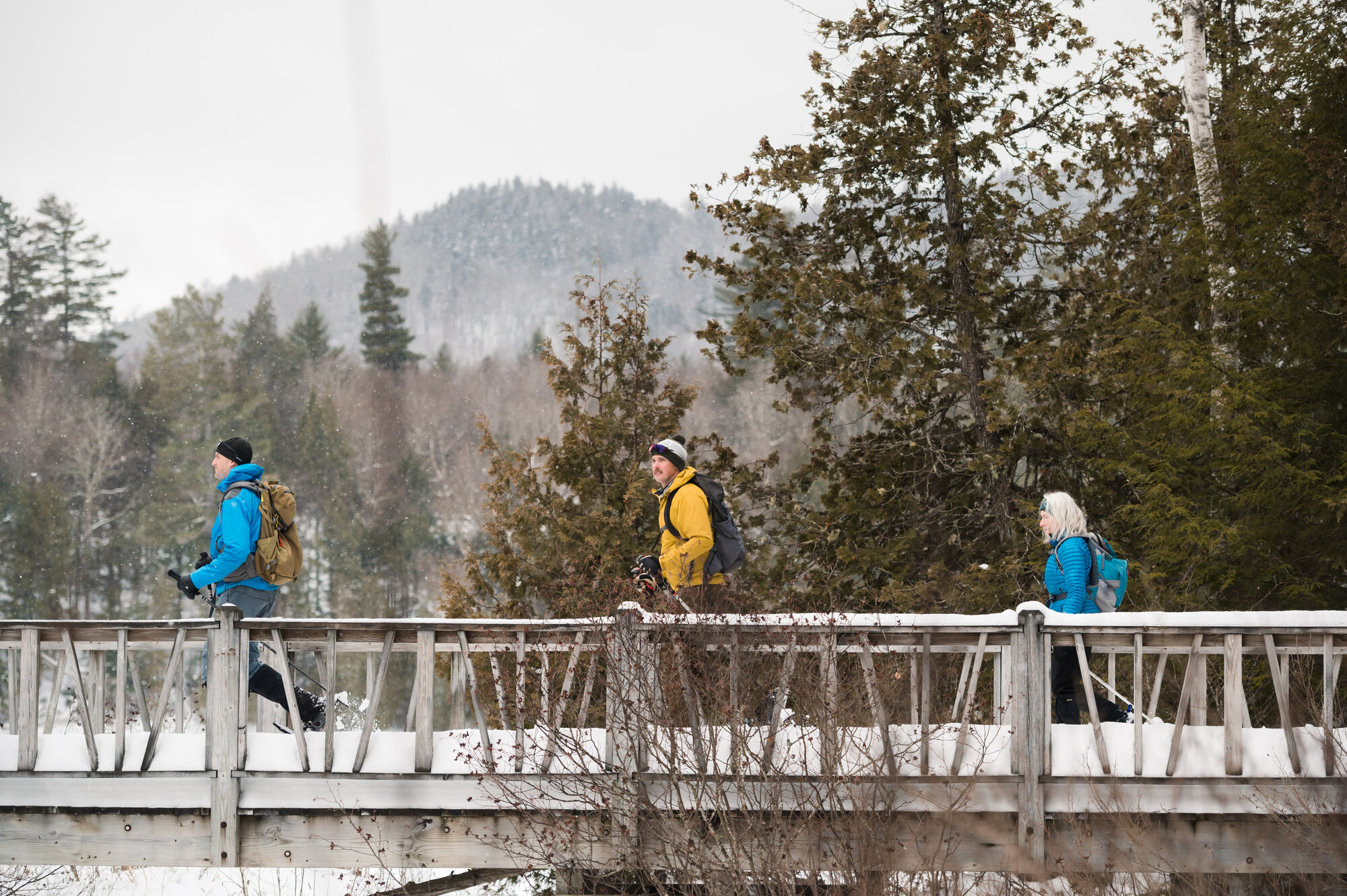 Three people walk a snowy bridge in winter. 