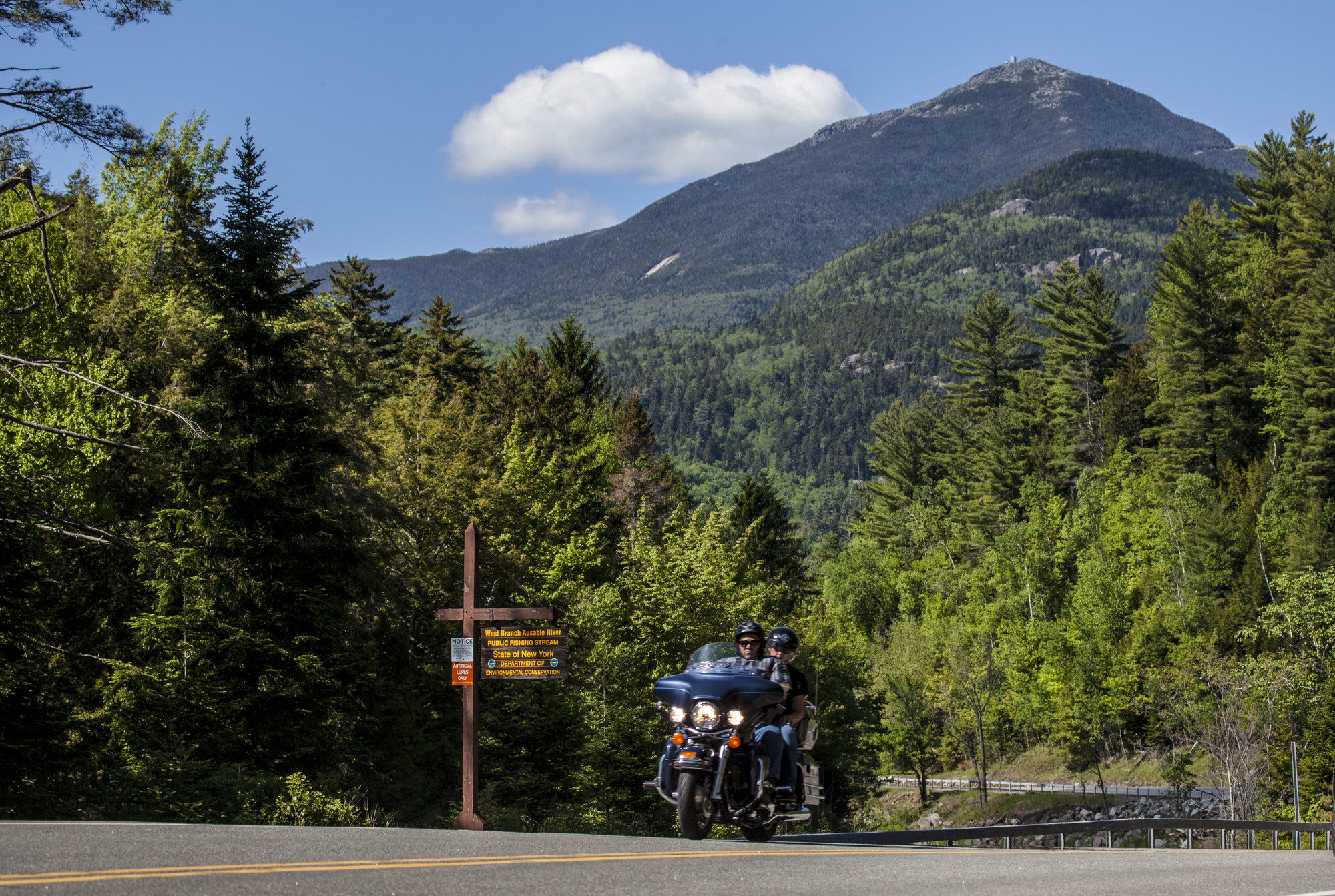Two people on a motorcyle riding with a mountain rising behind them.