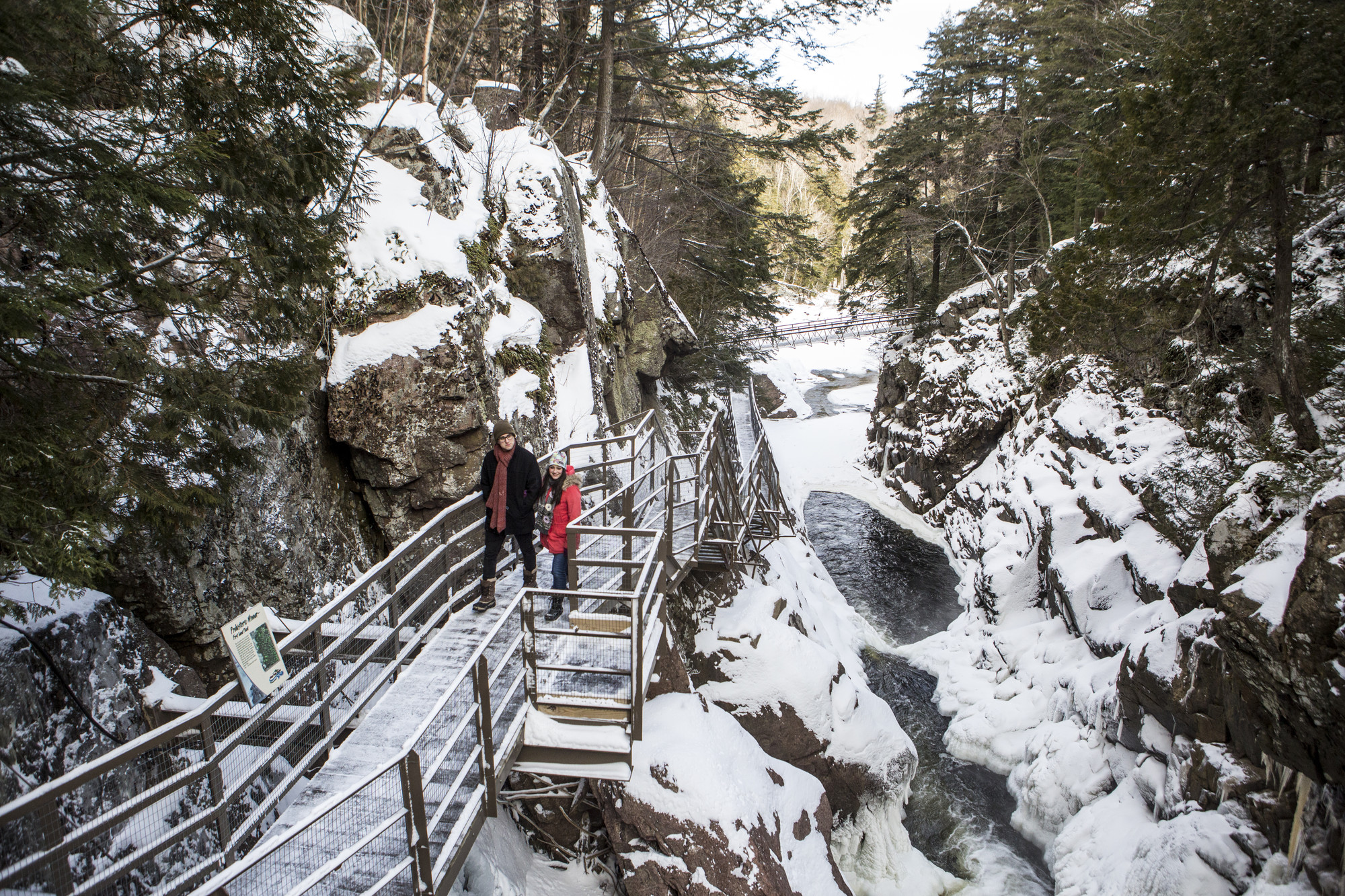 A man and woman walk on a pathway up a frozen waterfall.