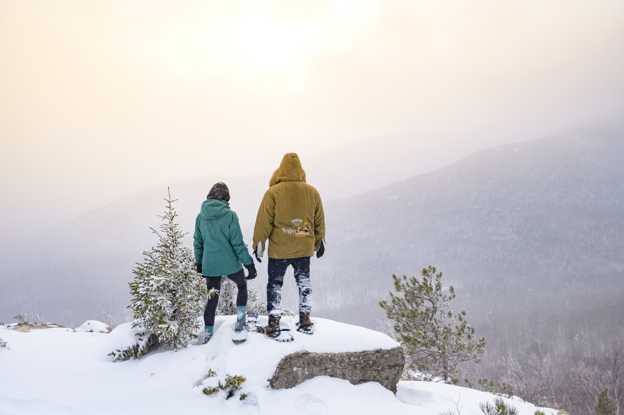A couple standing at the summit of a mountain while snowshoeing.