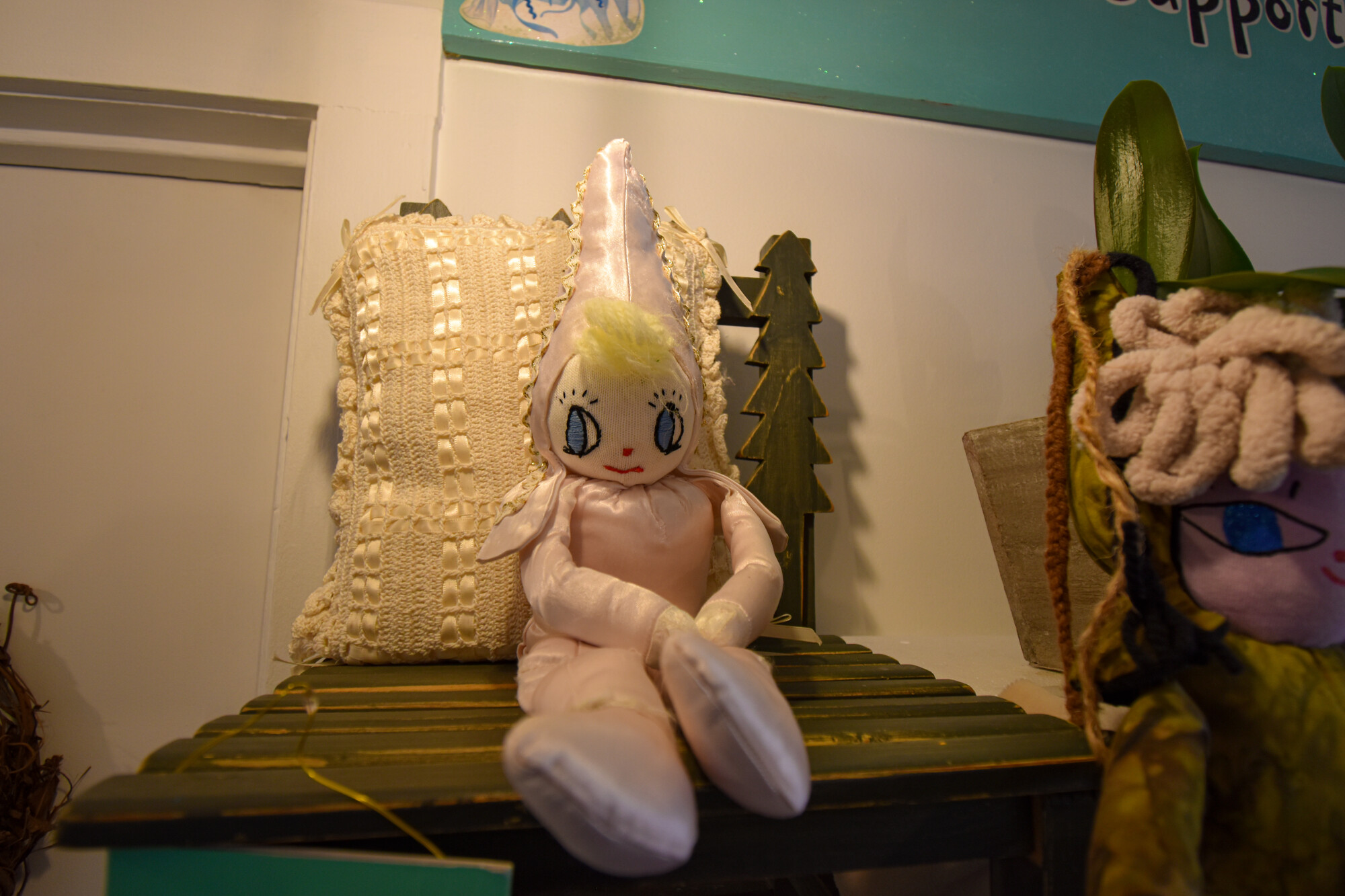 A handcrafted fairy doll wearing pink sits on a shelf in a shop.