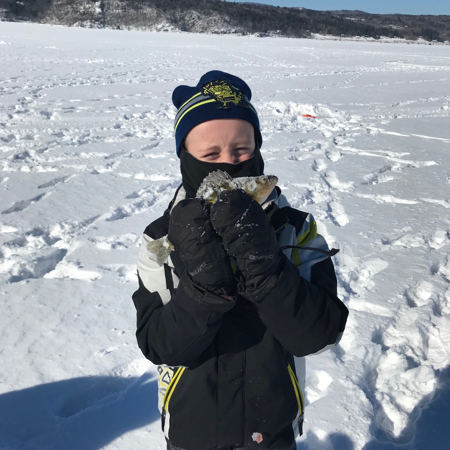 image of a young boy in parka and mittens holding a snowy fish