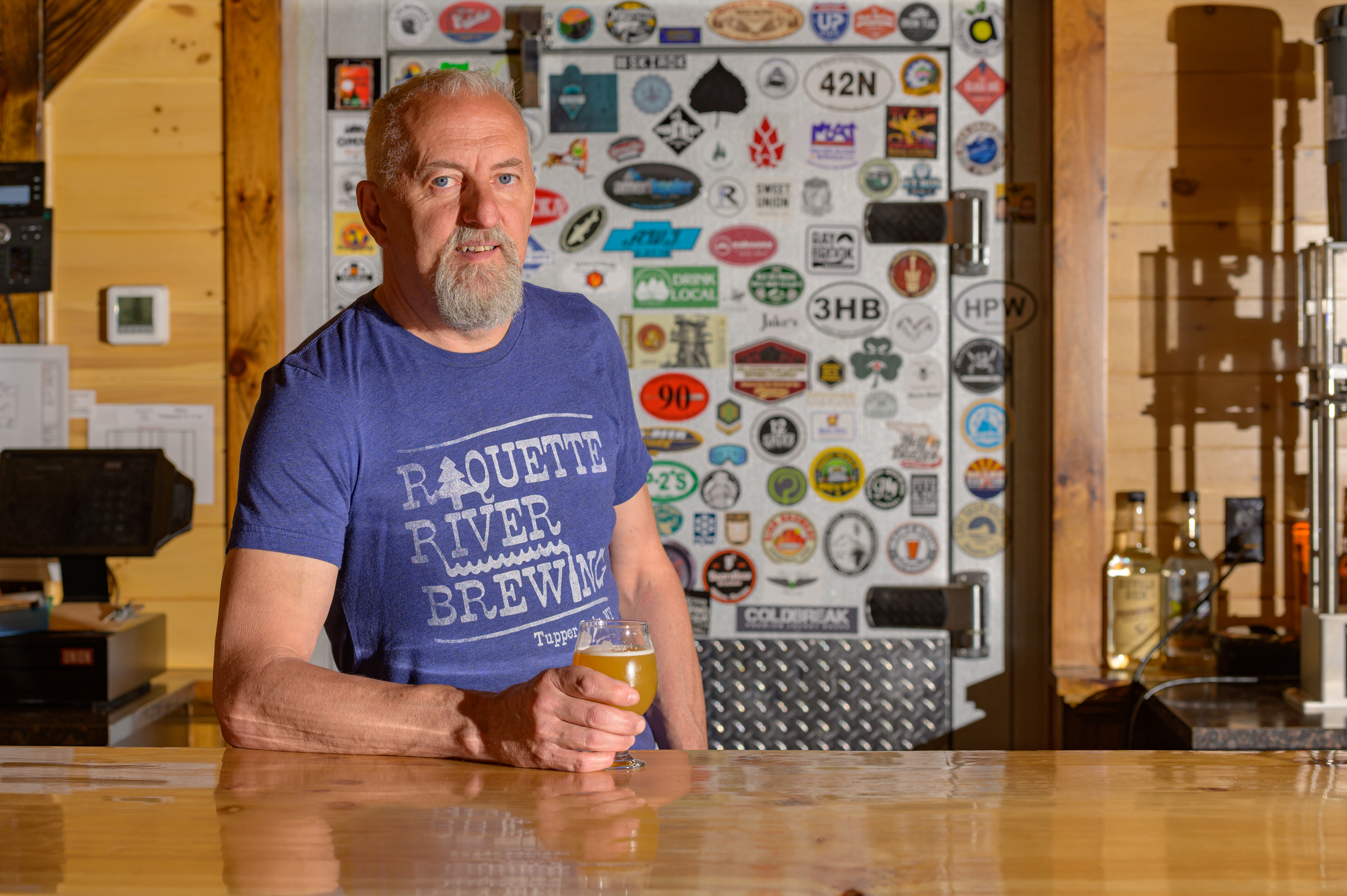 One of the owners of Raquette River Brewing poses behind the bar in the beer hall. 